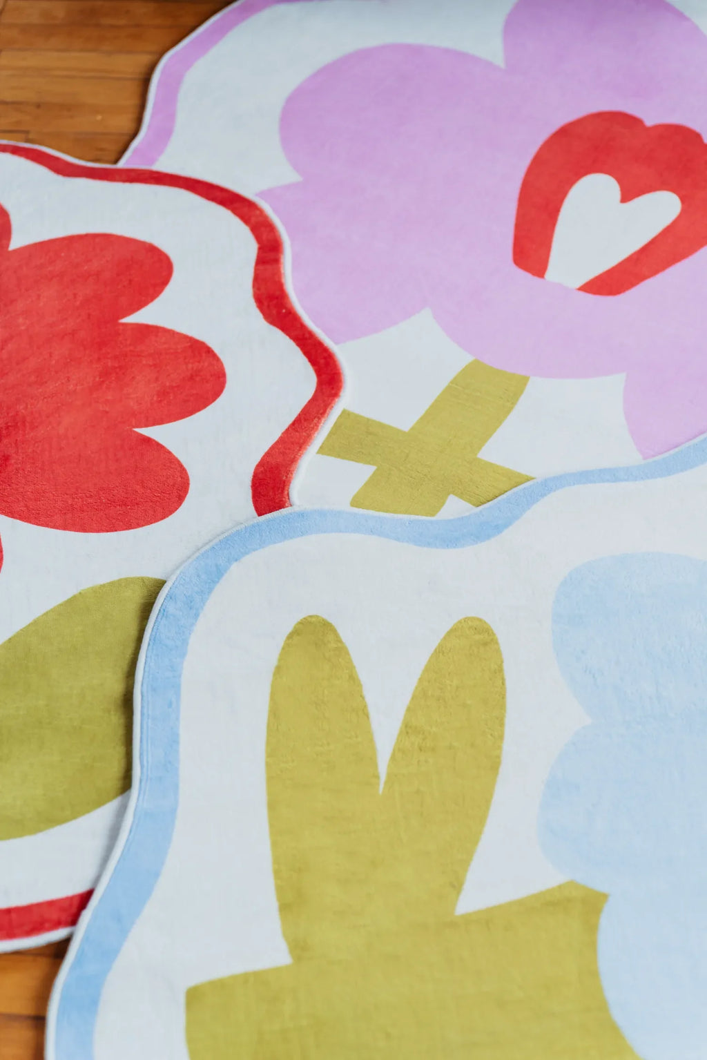 Close-up of overlapping flower rugs in orange, pink, and blue with bold playful patterns.