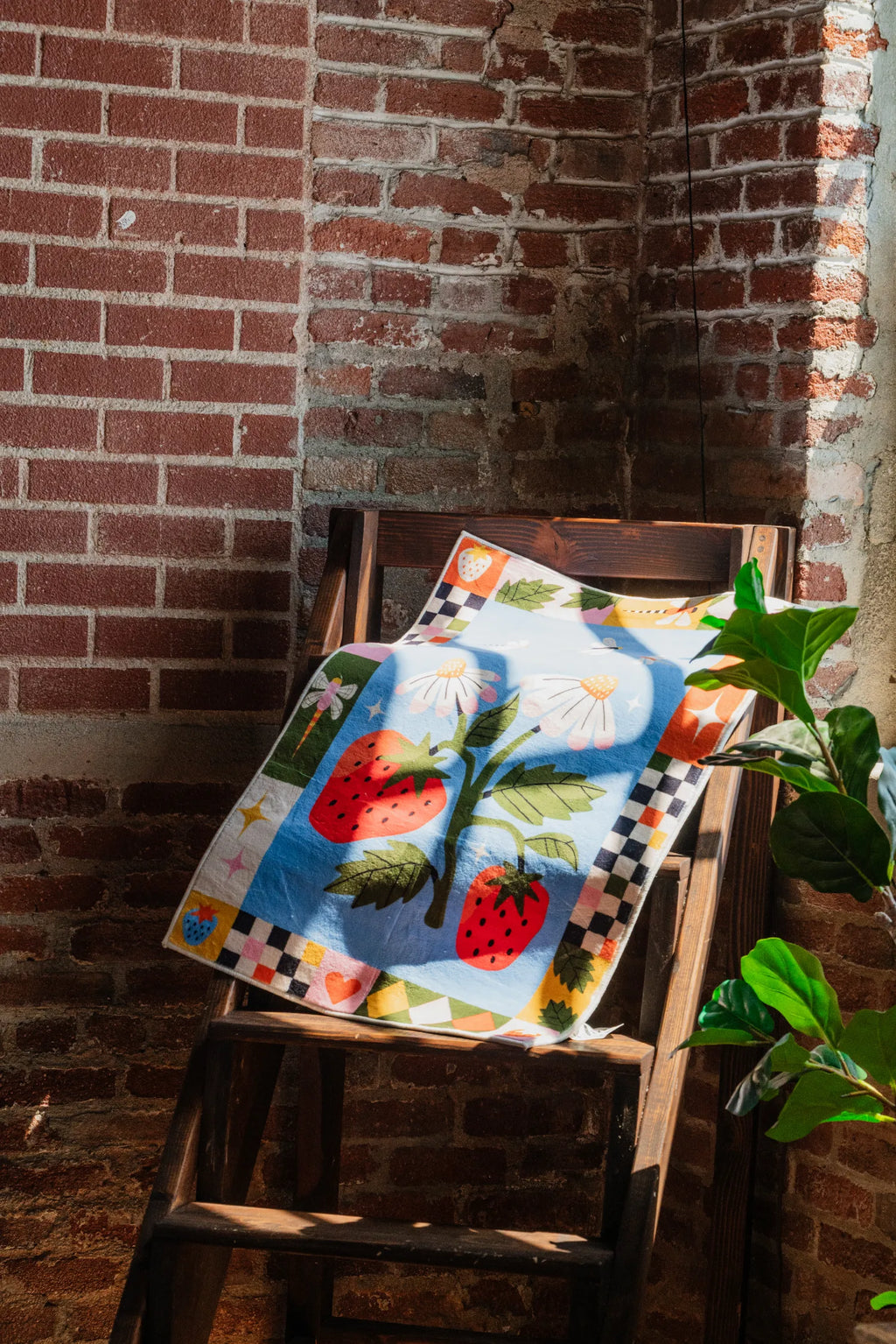Strawberry Patch Magic Rug draped on a rustic wooden chair near a brick wall adding playful accent to the room
