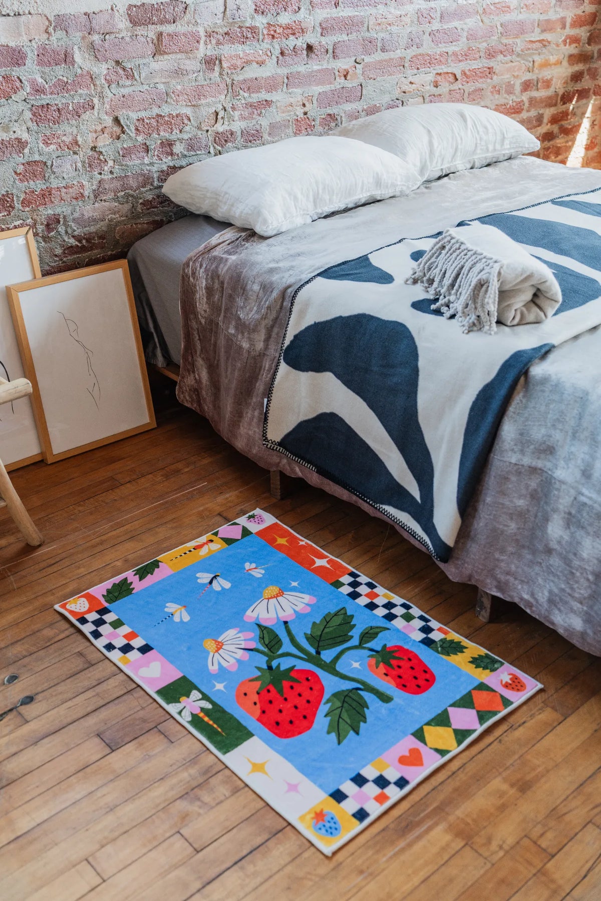 Strawberry Patch Magic Rug placed beside a cozy bed on wood floor in the bedroom with soft blanket styling
