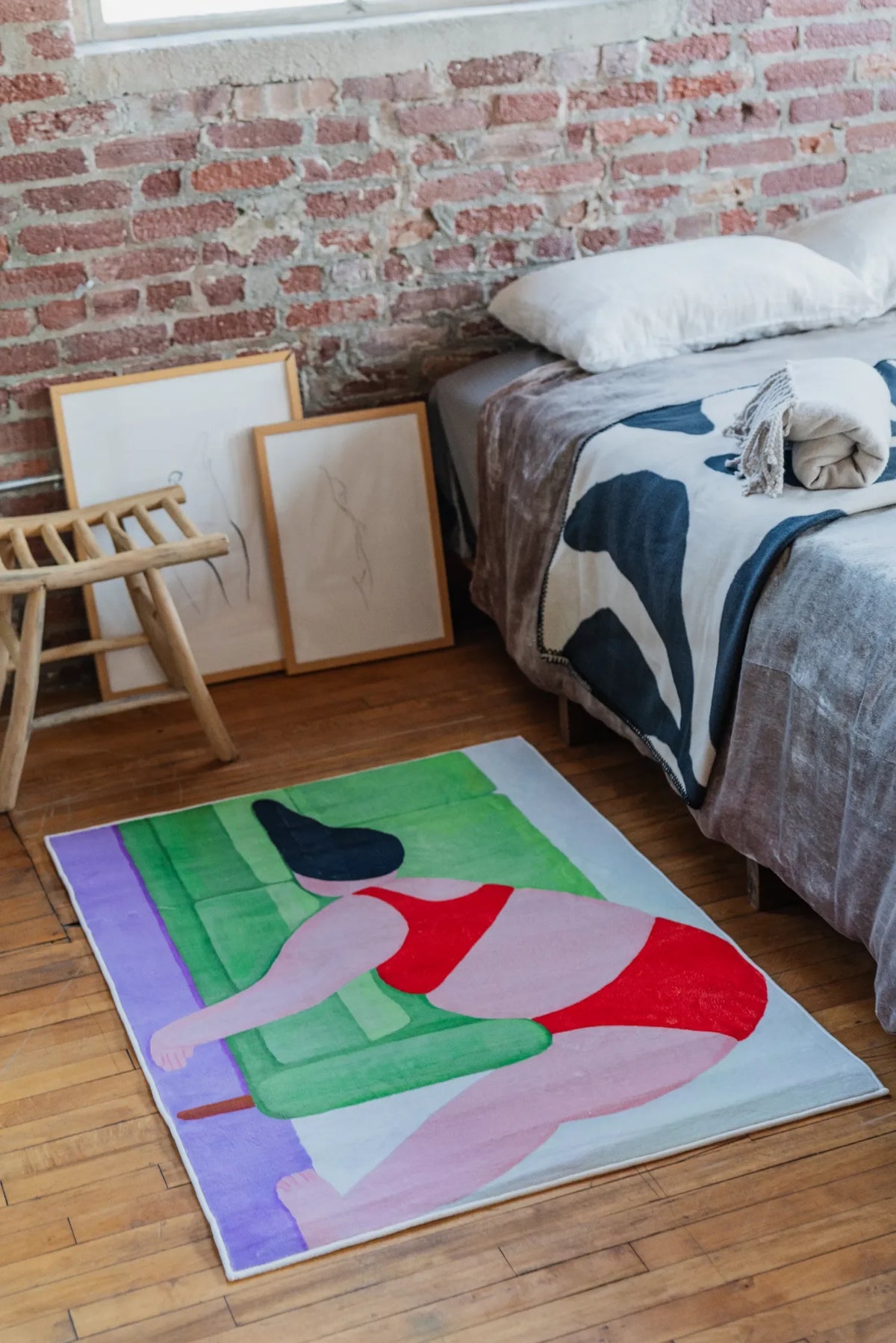 Modern Abstract Body Art Rug by Nimei set beside a minimal wooden chair and leaning frames, styled in a loft bedroom with exposed brick wall.