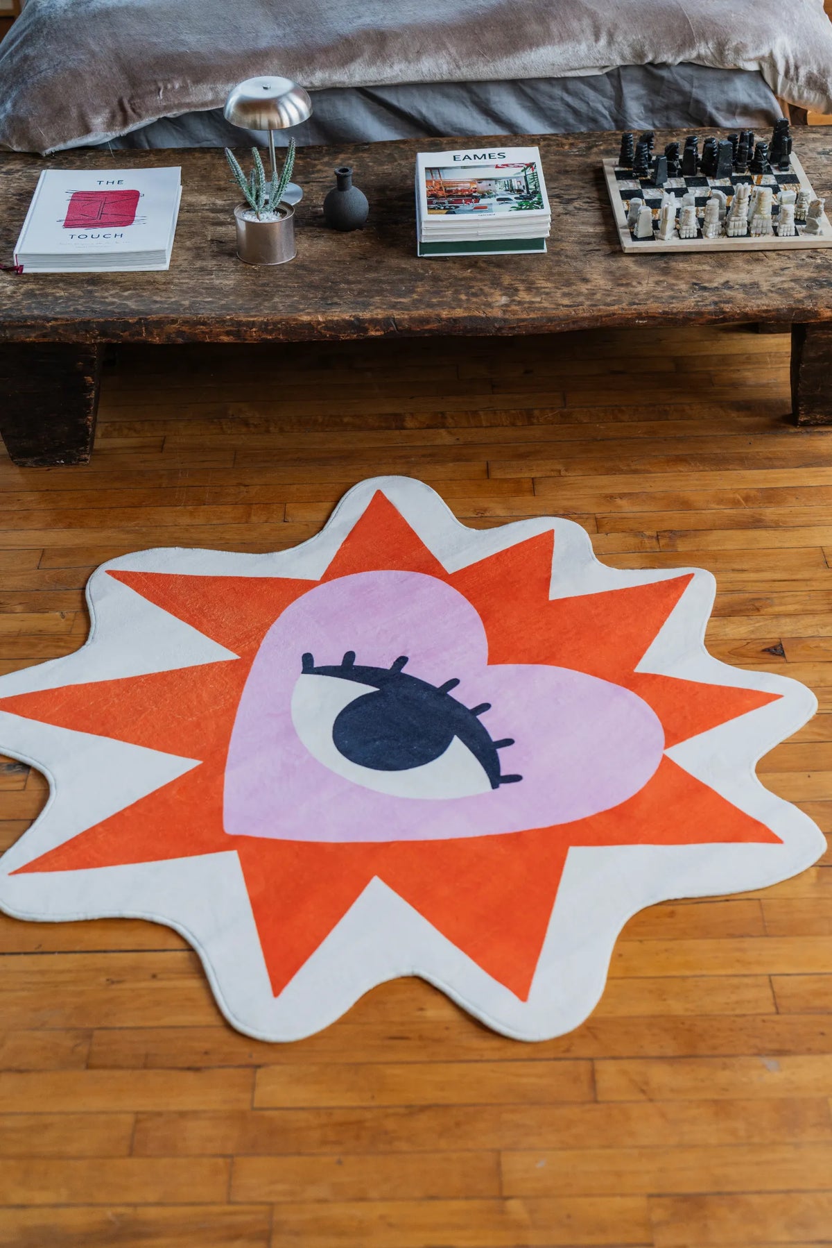 Decorative heart eye rug resting on wood floor with a rustic bench holding books in the background