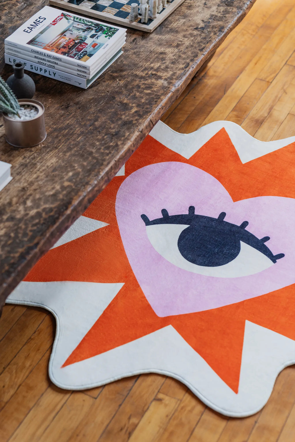 Heart Eye Rug by Megan Roy partly tucked under a rustic bench with books on wood floor
