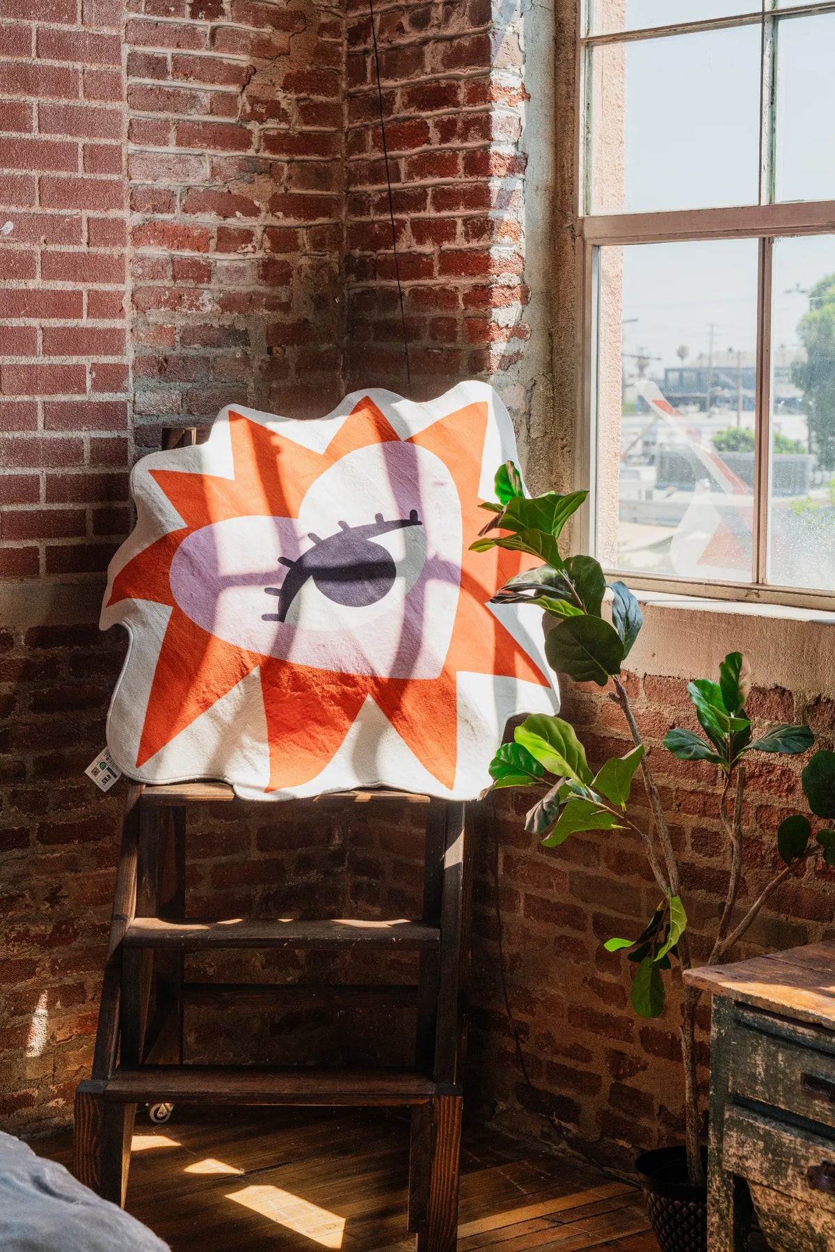Heart Eye Rug draped over a wooden chair beside a brick wall and sunlit window
