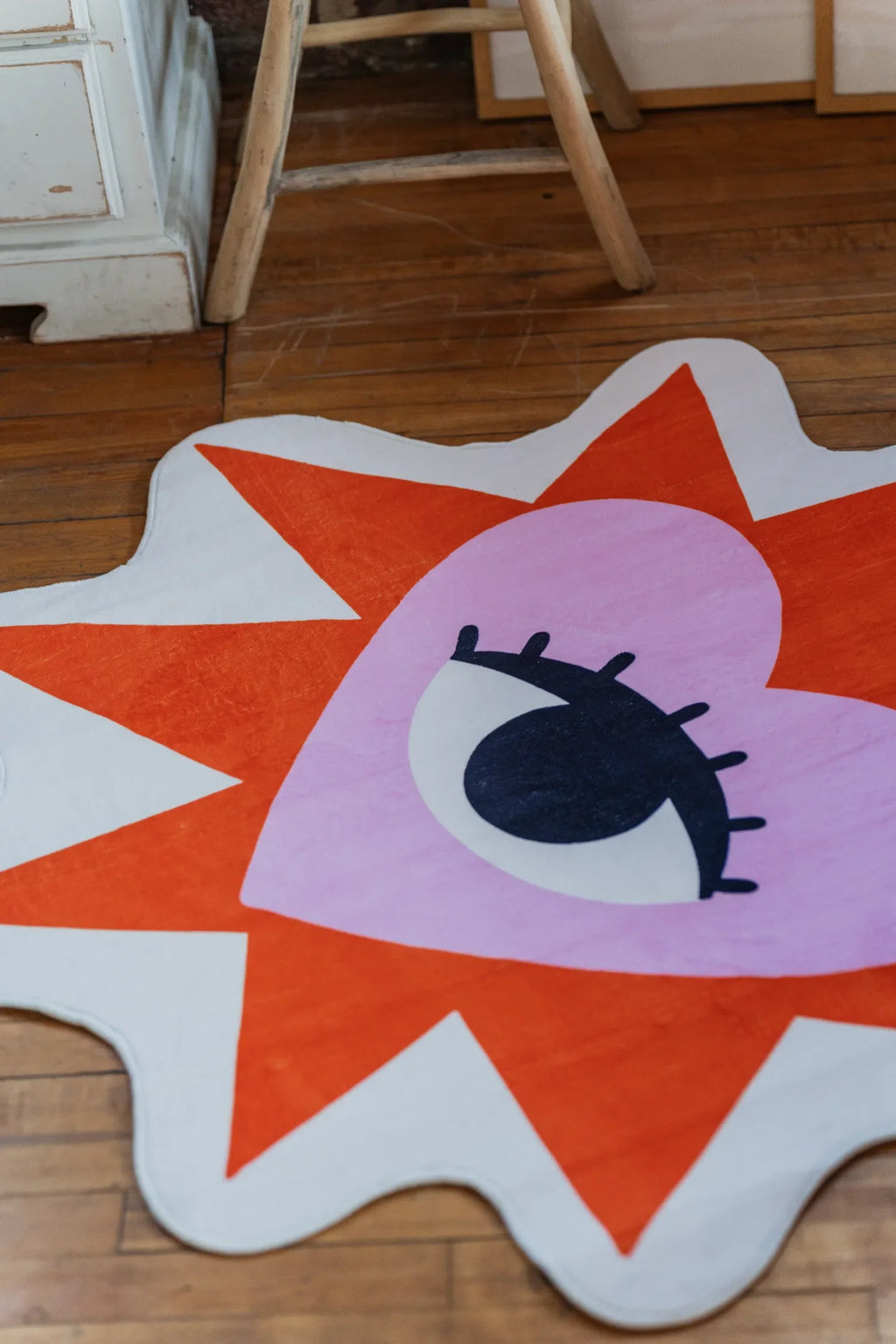 Decorative heart eye rug in bold colors resting on wood floor near a wooden chair