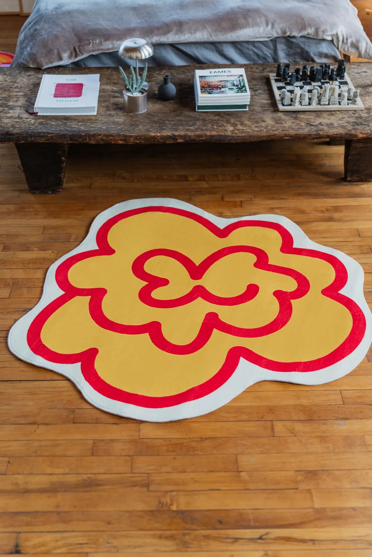 Yellow Funky Flower Shaped Irregular Rug by the bed rests on wood floor, becoming a bright focal point beside a rustic table.