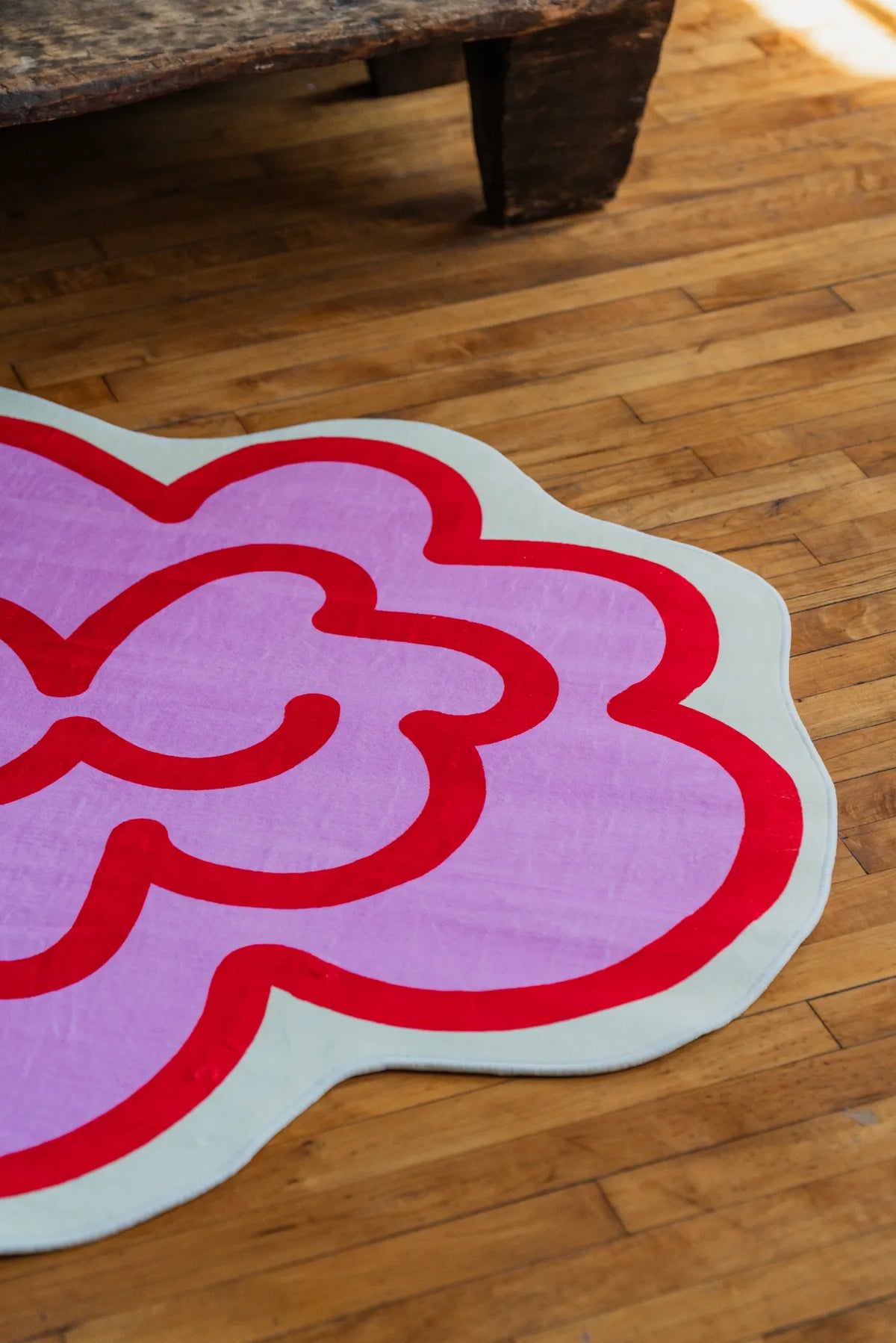 Close-up of pink Funky Flower Rug placed by a vintage table, the modern area rug softens the warm wood floor below.