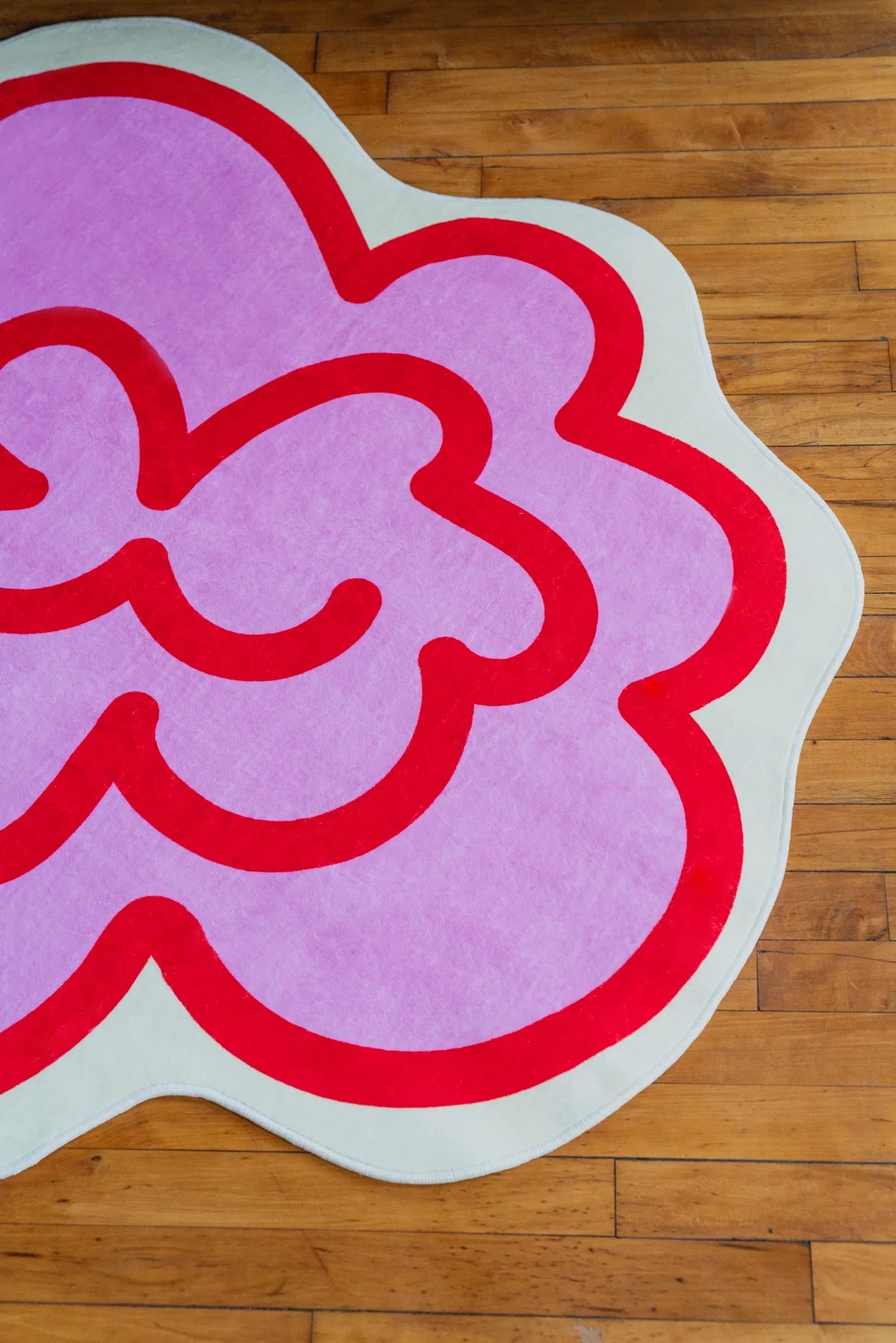 Bright pink funky rug with bold red trim lying across polished wood floor, a lively detail that energizes the cozy corner.