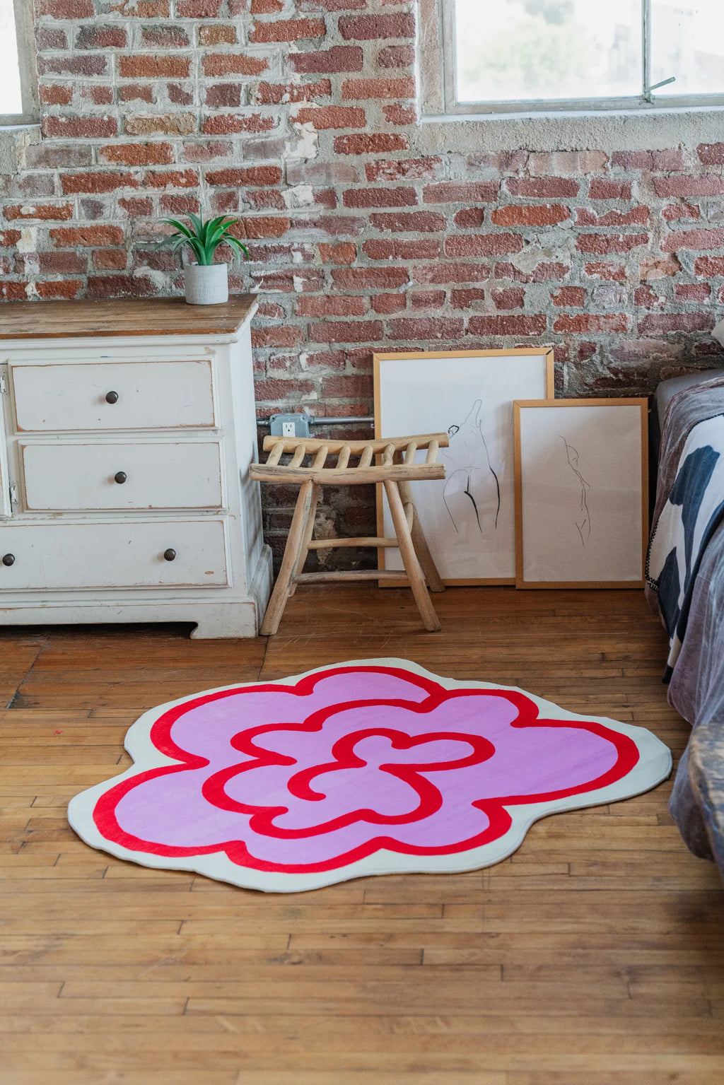 Pink funky flower rug beside a rustic chair and dresser, adding playful charm to a brick wall bedroom.