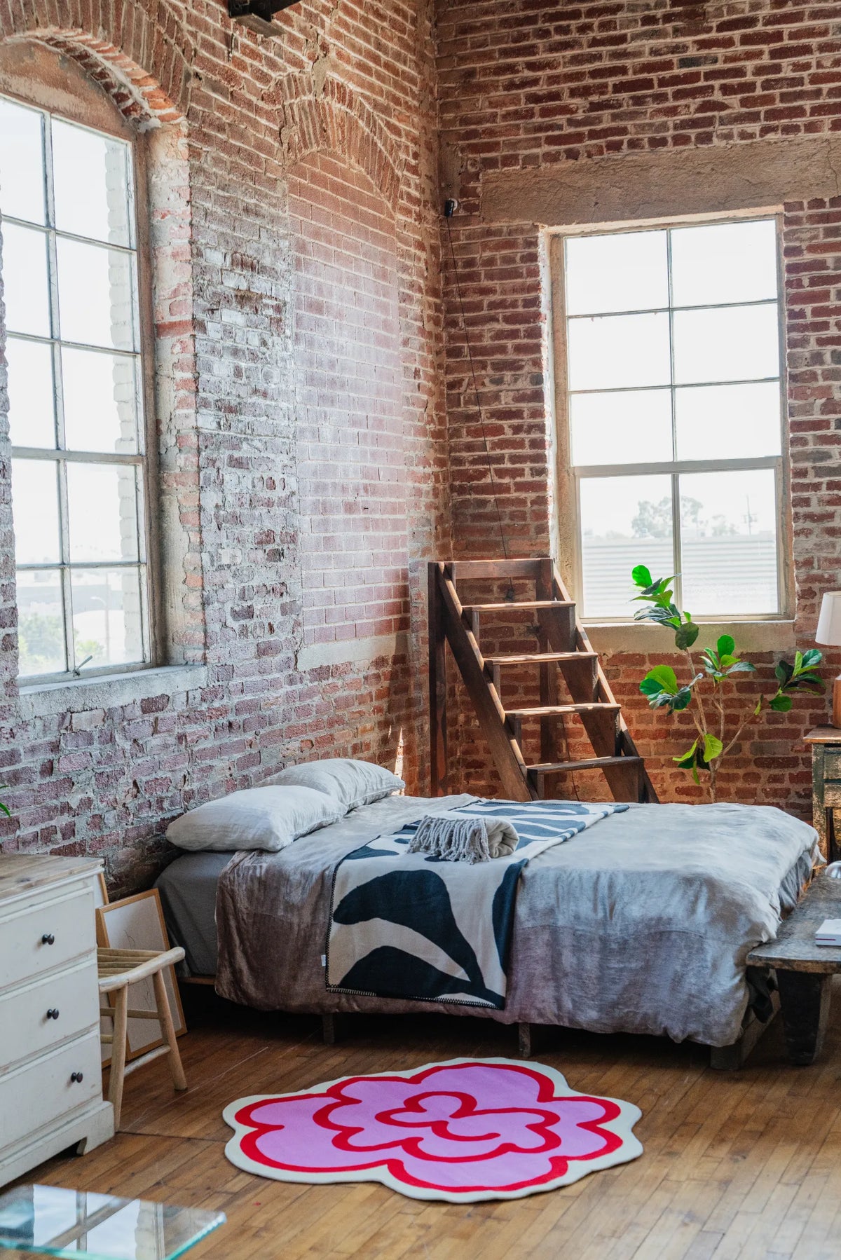 Funky flower rug in pink set near a low bed and tall window, brightening the loft style bedroom space.