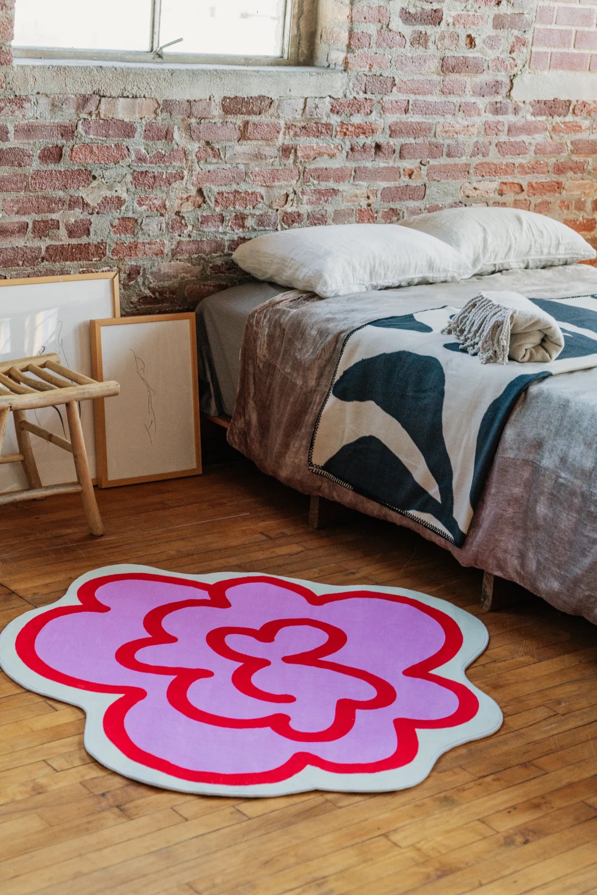 Pink funky flower rug placed next to framed art and wooden stool, creating a cozy accent by the bedside.