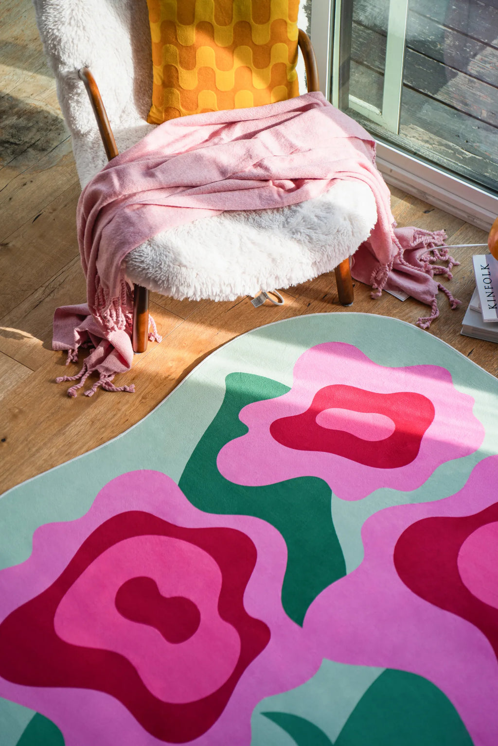Close-up of the floral rug’s vivid pink and red blooms next to a shearling chair and glass door on wood floor.