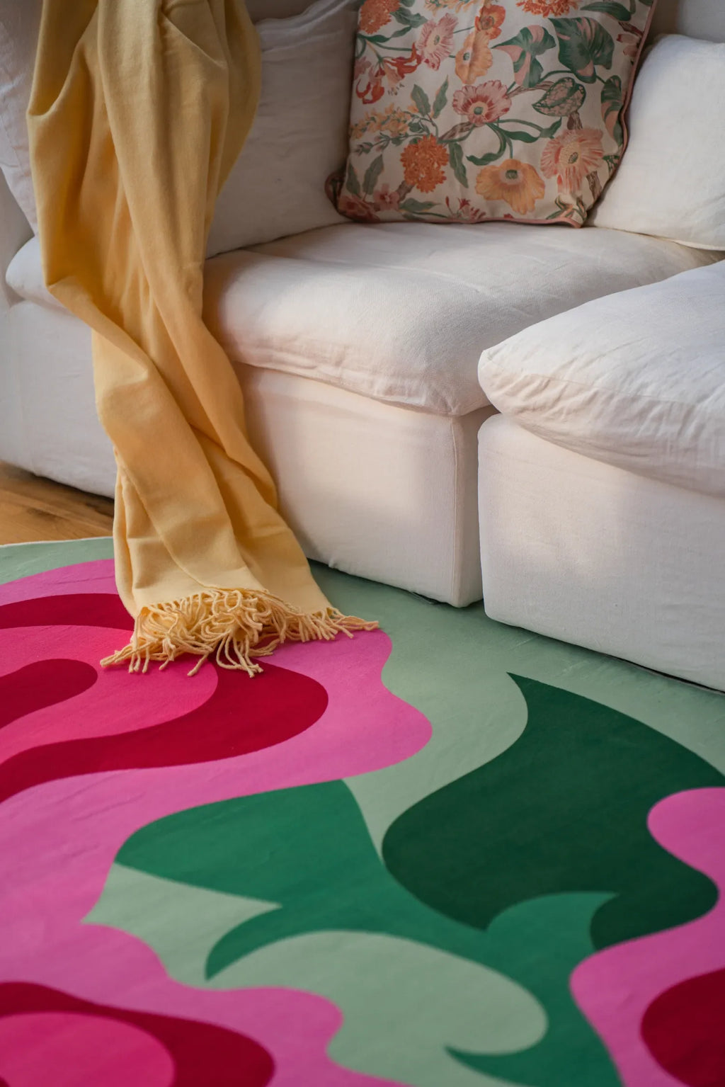 Green and pink floral rug tucked under a white sofa with patterned pillows on wood floor in soft natural light.