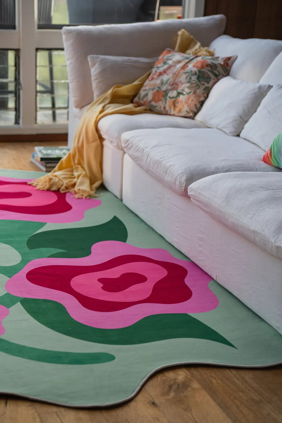 Floral rug with abstract rose shapes stretching out in front of a large white couch on light wood floor.