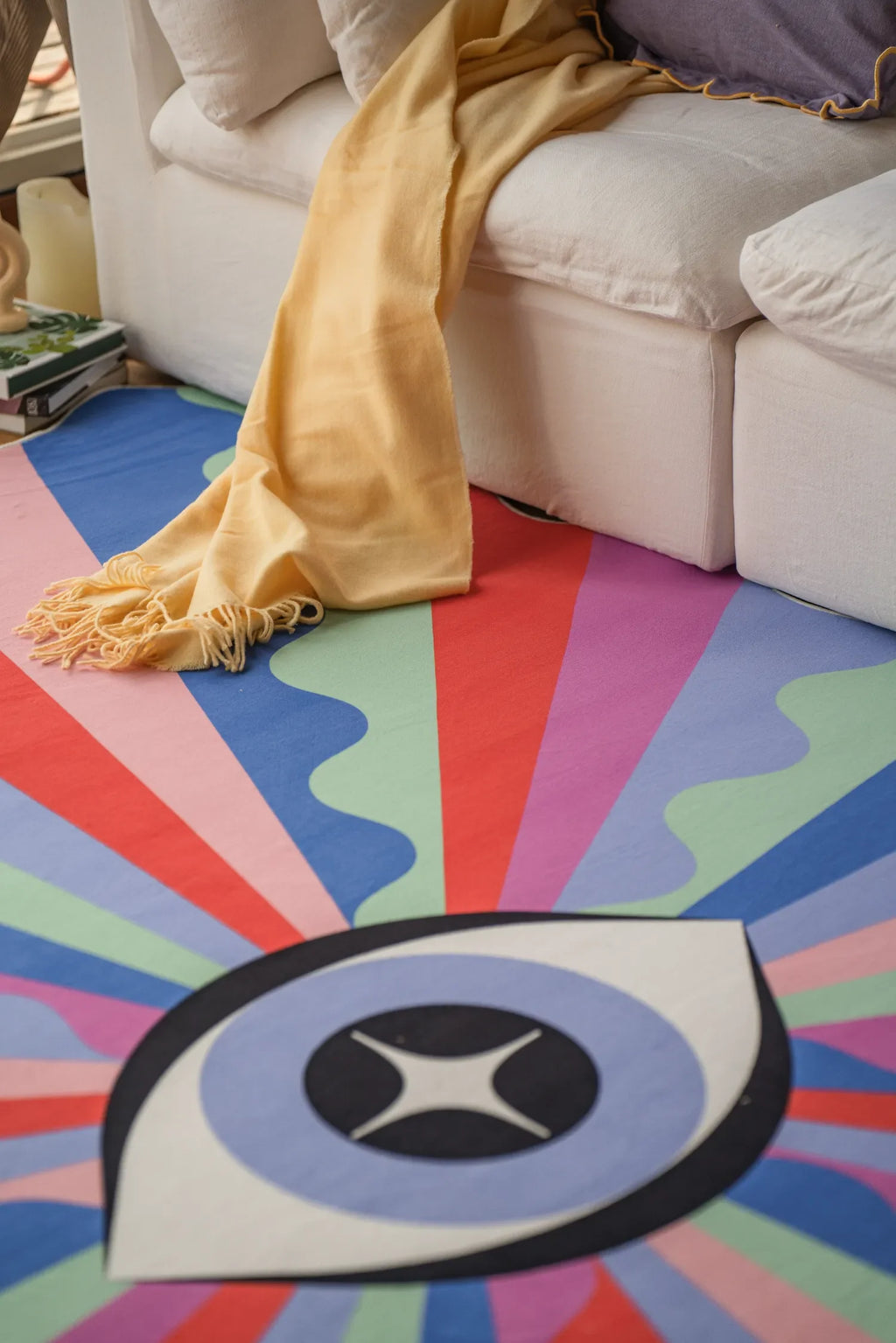 Colorful Lazer Rays Eye Rug placed partly under a cream sofa, its bold rays fanning out across the wooden floor.