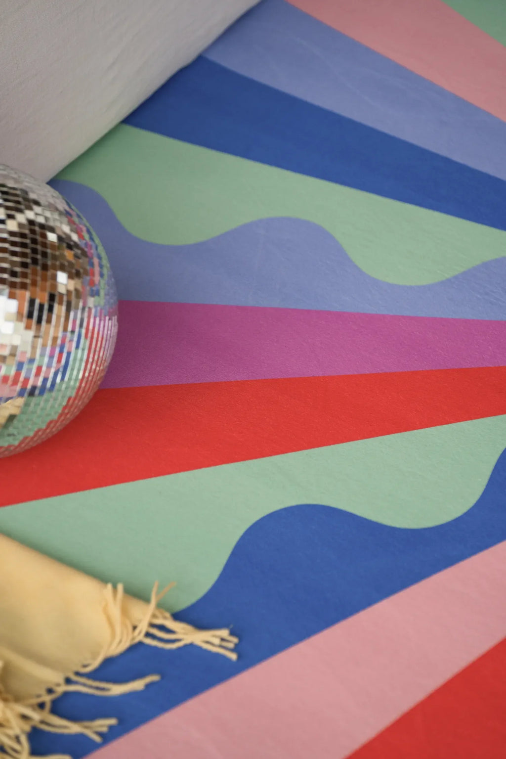 A close-up of the wavy colorful rug with laser ray stripes in purple, red, and mint green, tucked beneath a modern sofa.