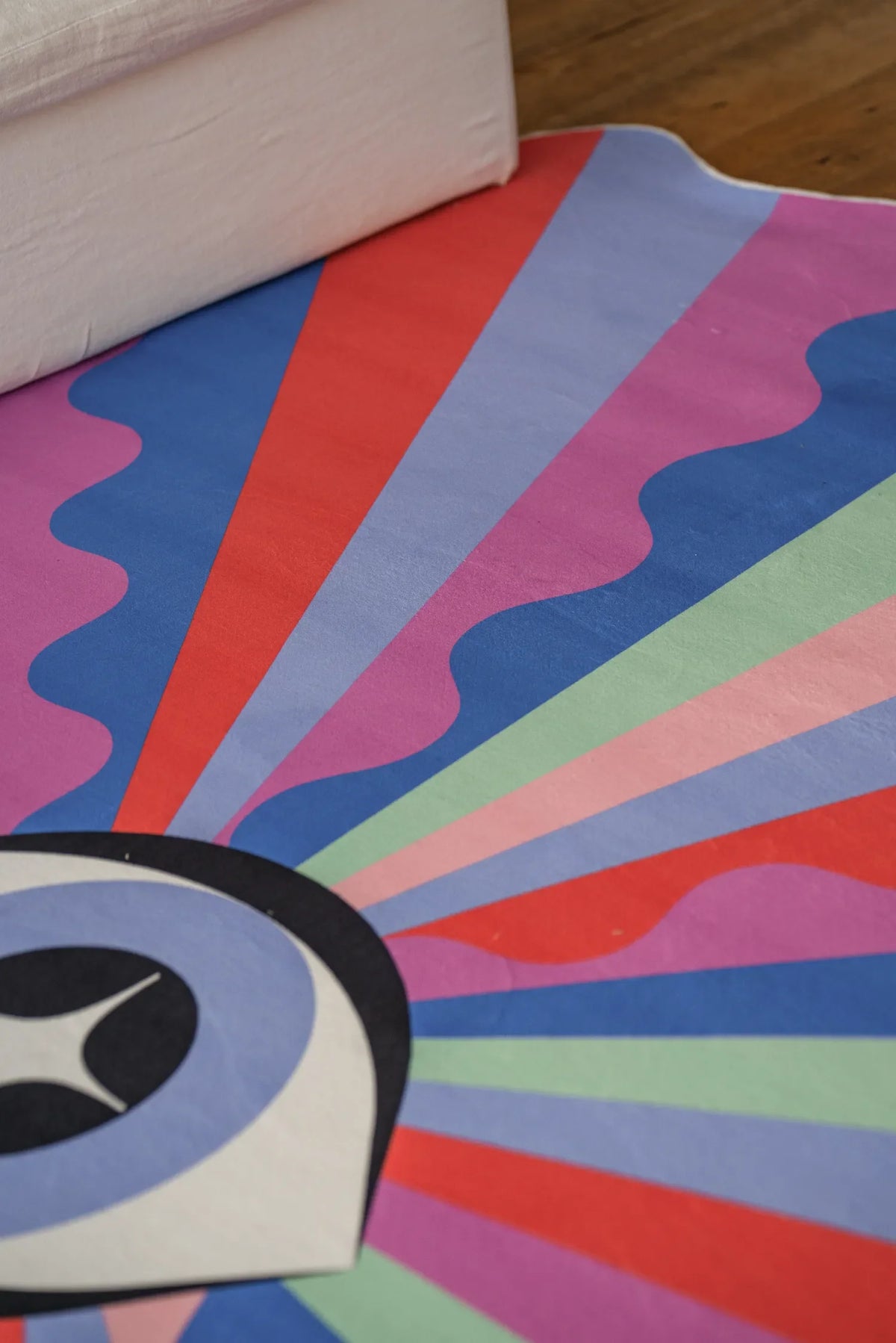 Detail of the Colorful Lazer Rays Eye Rug by Jessica Miller near a white sofa on wood floor