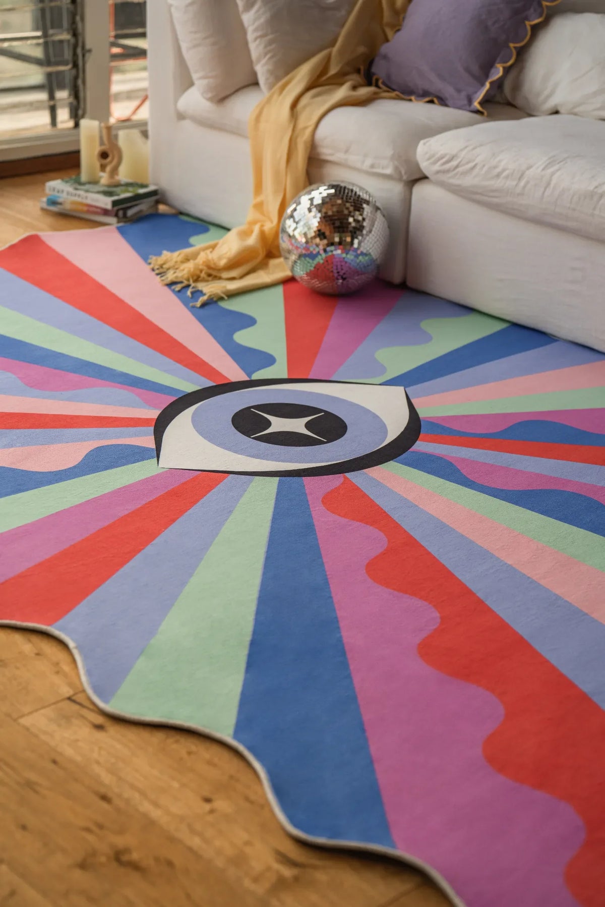 Colorful eye rug spread out in a cozy nook beside a white couch on hardwood floor