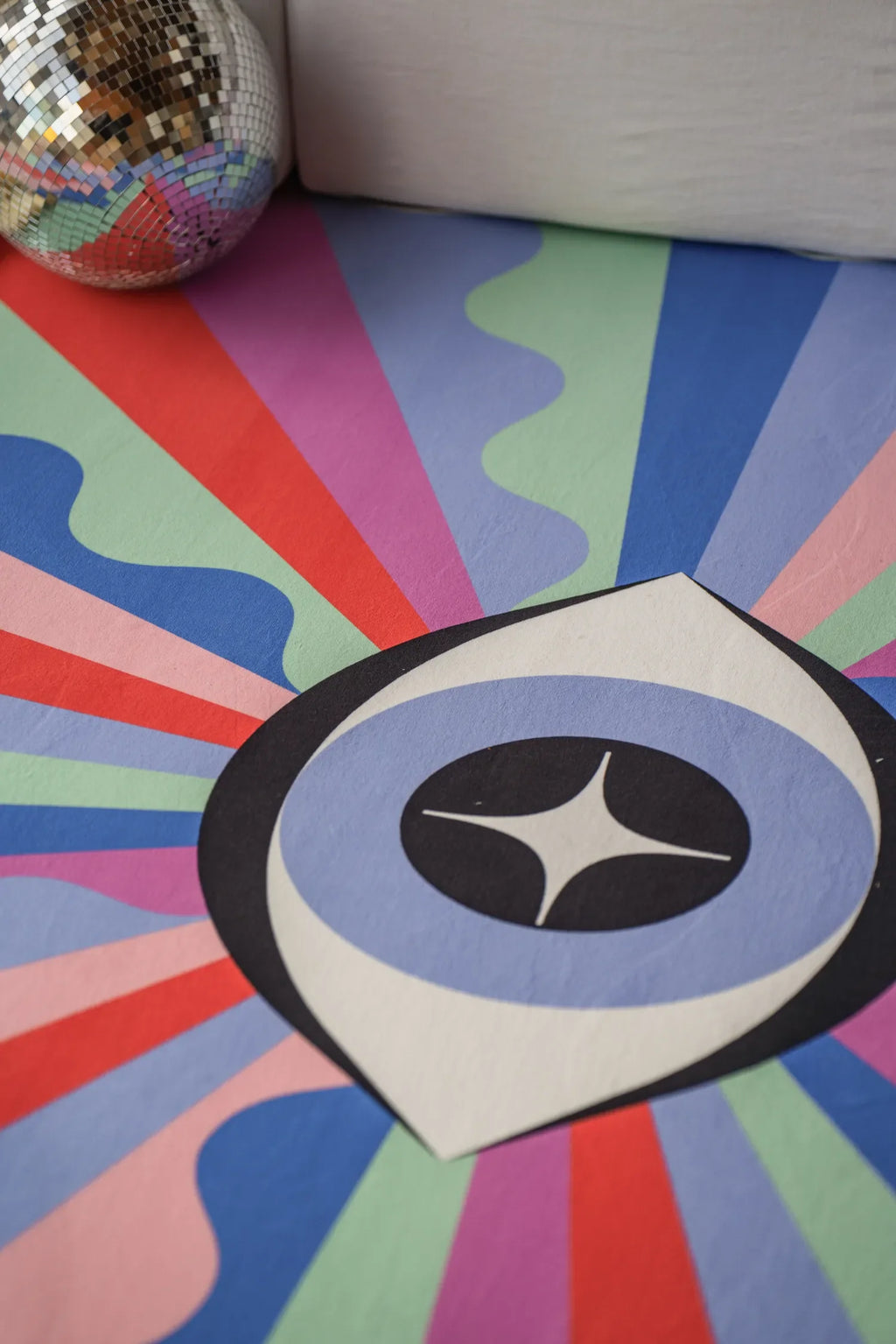 Detail of the colorful Lazer Rays Eye Rug showing radial stripes and central eye pattern on wood floor.
