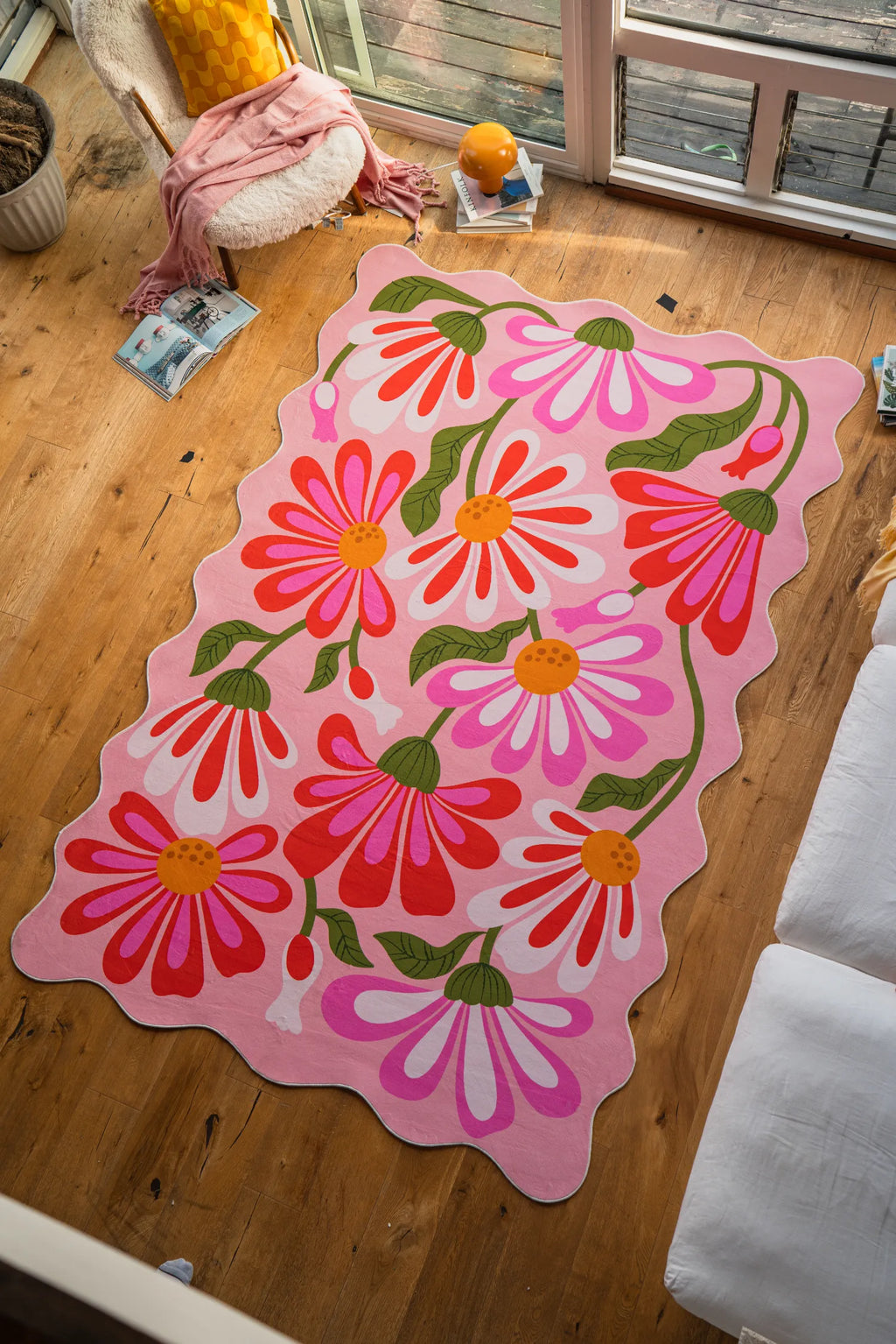 Pink floral wavy rug by Jessica Miller laid out on wood floor beside a sofa in the living room.