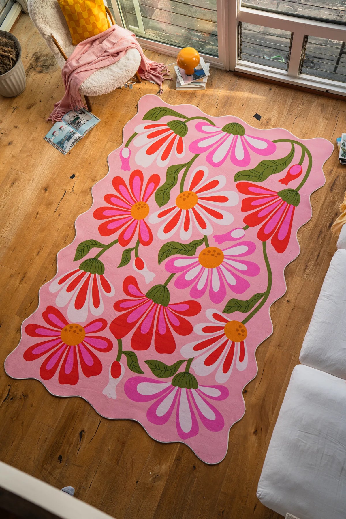 Pink floral wavy rug by Jessica Miller laid out on wood floor beside a sofa in the living room.