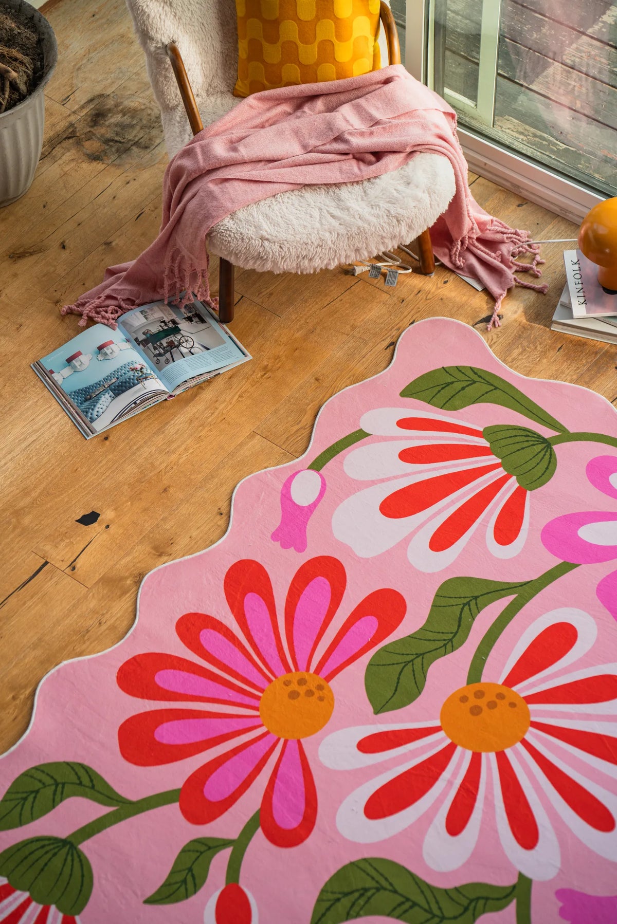 Pink floral wavy rug beside a sherpa chair near tall windows in a quiet reading corner.