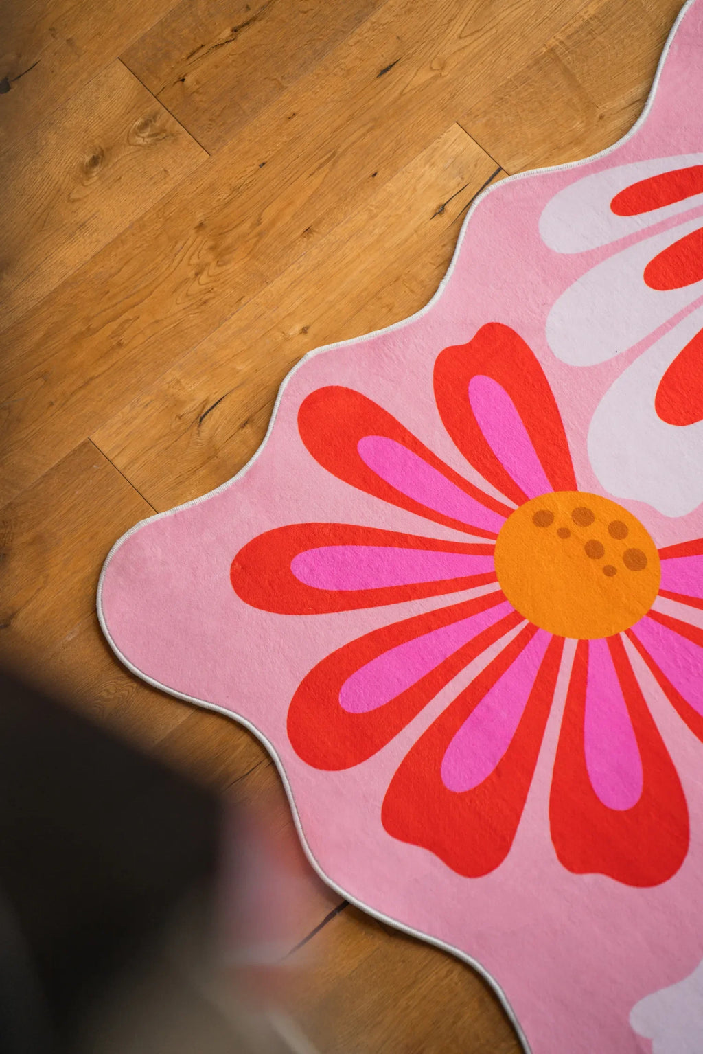Scalloped edge of a pink floral wavy rug on natural wood flooring in soft daylight.