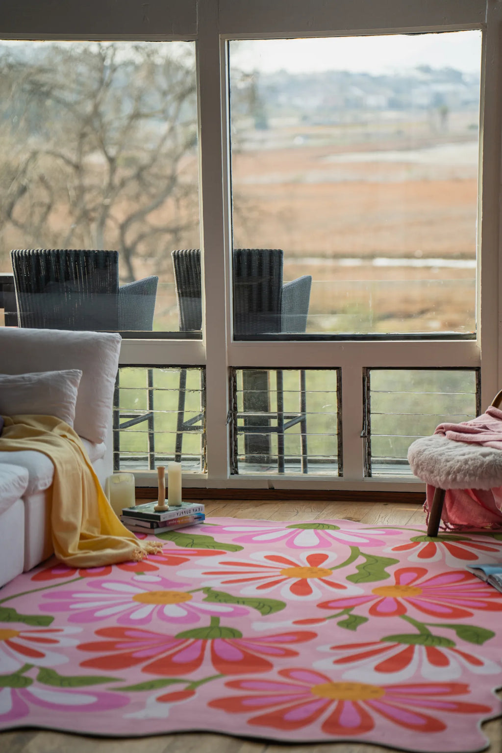 Pink floral wavy rug placed in front of large windows beside a sofa in a sunlit living room.