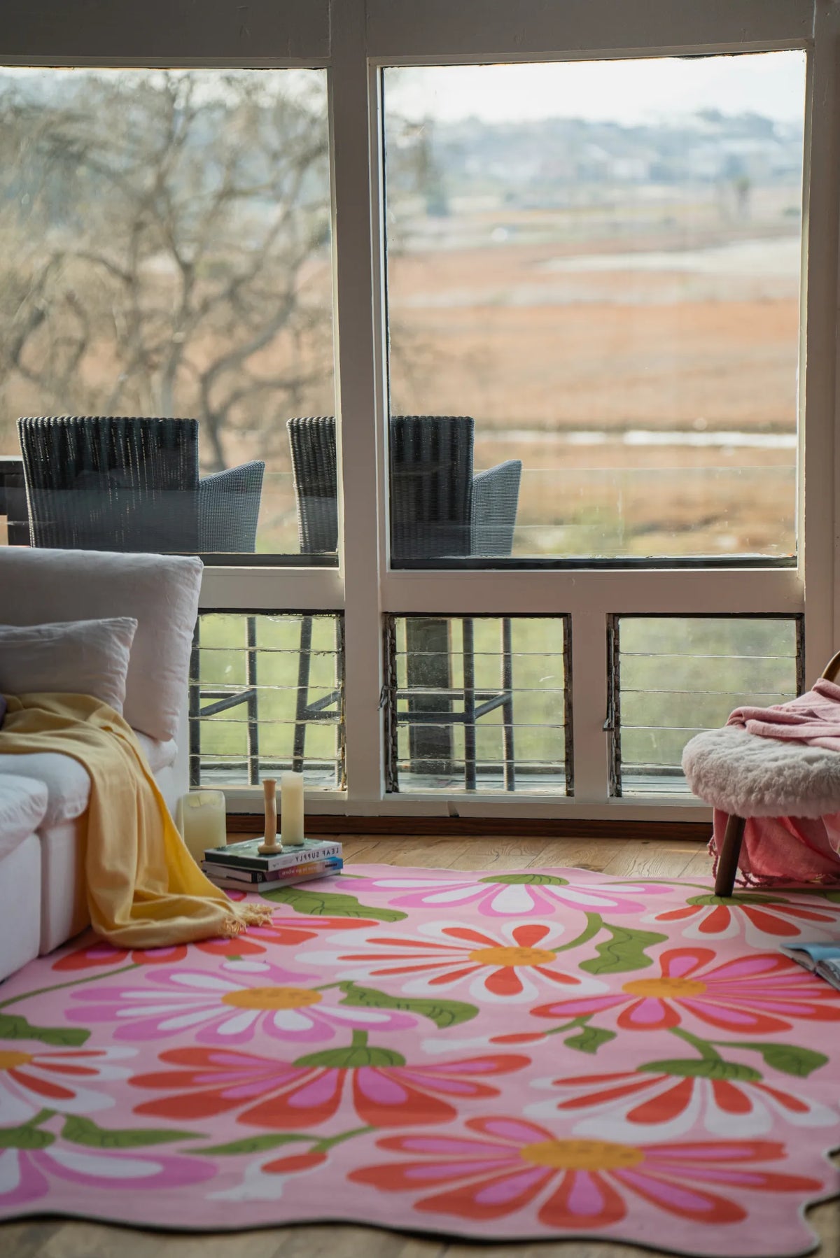 Pink floral wavy rug placed in front of large windows beside a sofa in a sunlit living room.