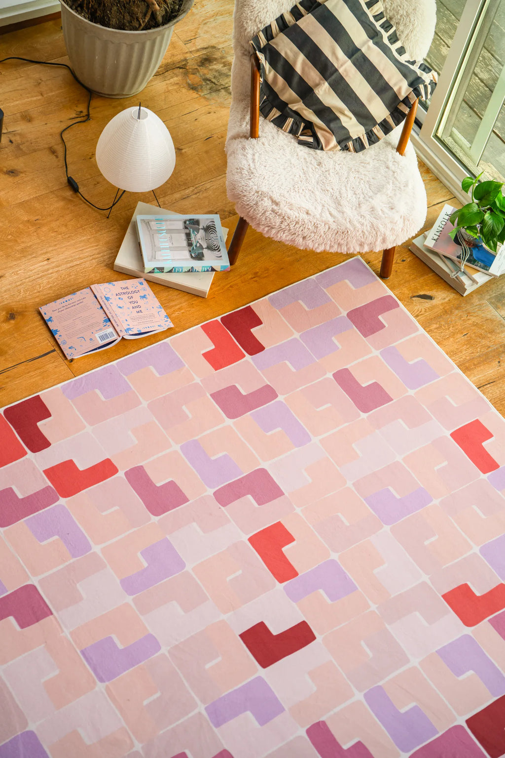 Pink pastel rug beside a sherpa armchair and books on wood flooring in the living room.