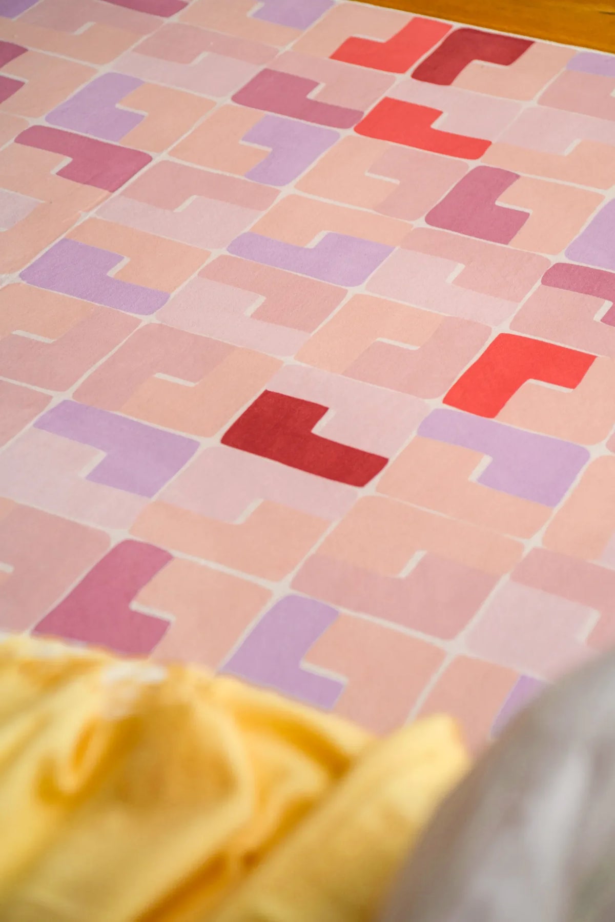 Close-up of pink pastel mosaic rug with geometric tiles in soft red, lilac, and peach tones.