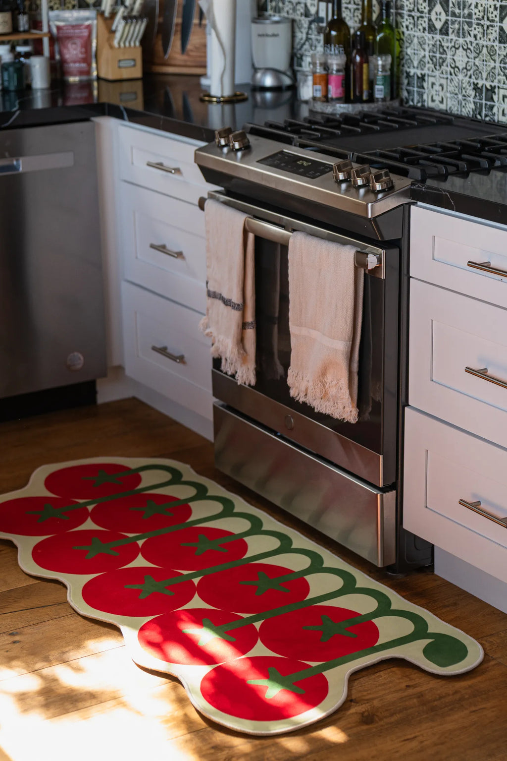 Playful tomato-shaped rug by Johann Banta brightens up the kitchen floor, placed in front of a modern stove and white cabinets.