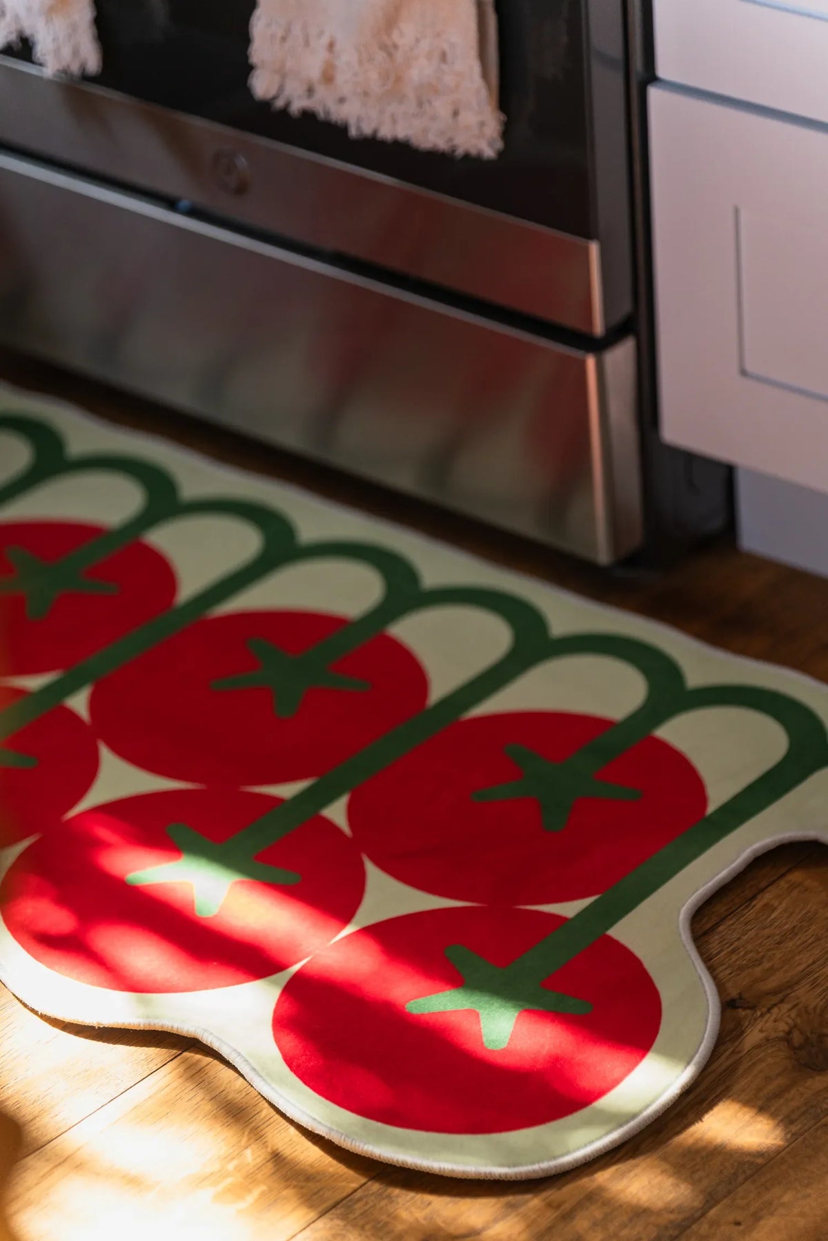 Close-up of the irregular tomato rug’s vibrant red and green detailing, catching natural light on a wooden kitchen floor.