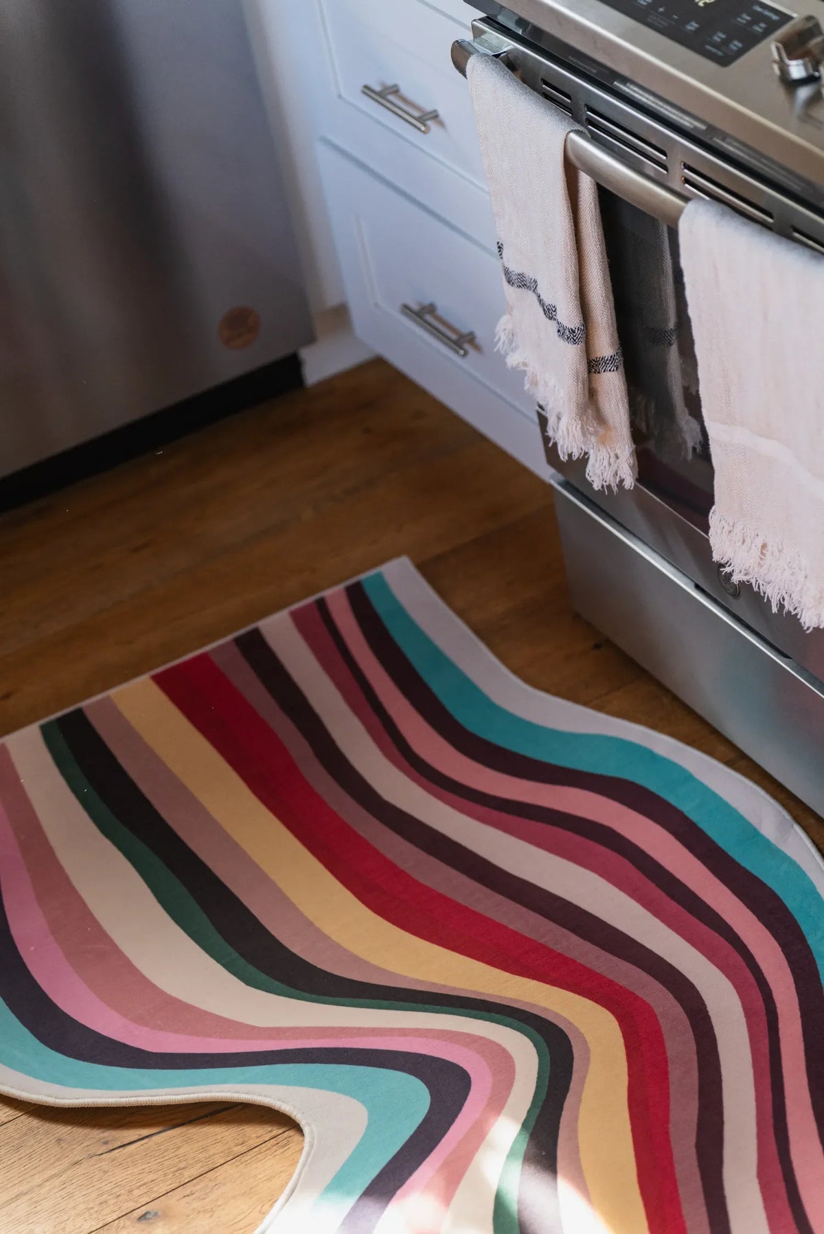 Closer look at multicolor contour rug in kitchen, with pink, red, teal, and yellow waves near stainless steel appliances.
