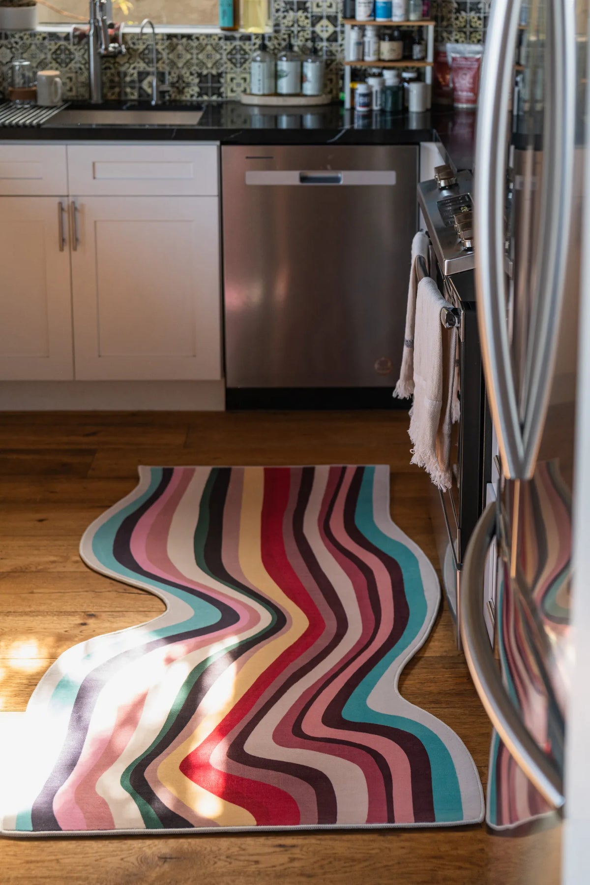 Wavy multicolor contour rug in sunlight-filled kitchen, placed between stainless steel fridge and white lower cabinets.