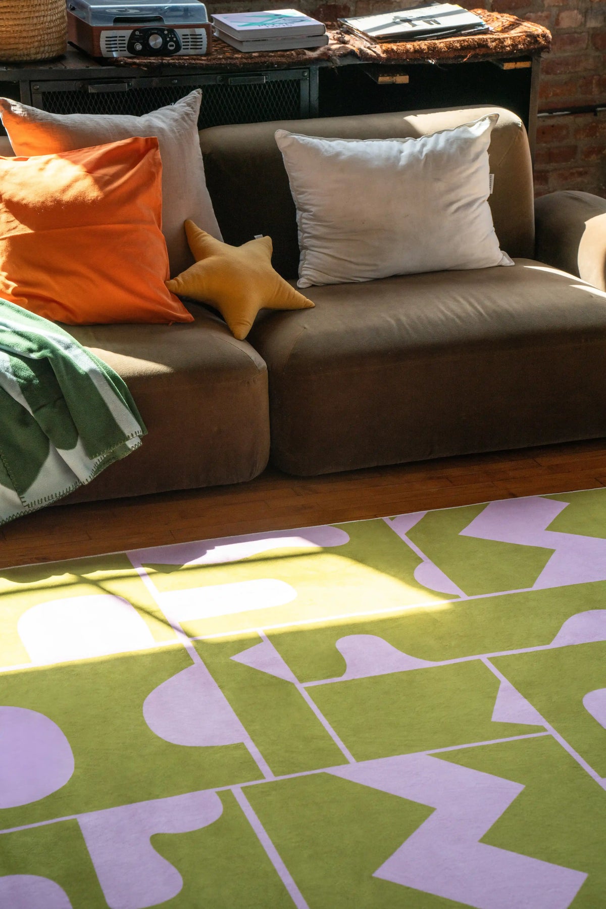 Close-up of olive green Abstract Patchwork Rug next to brown couch and throw pillows in modern apartment decor