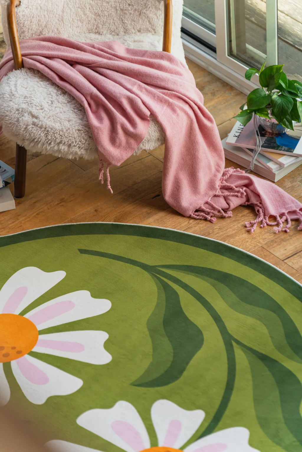 Close-up of the daisy rug edge near a chair and potted plant by the window in the living room.