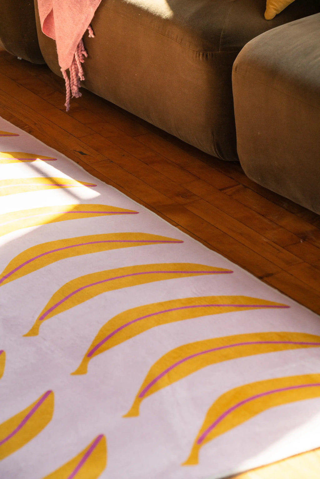 A playful runner with bright banana motifs sits in front of a deep-toned sofa on a wood floor