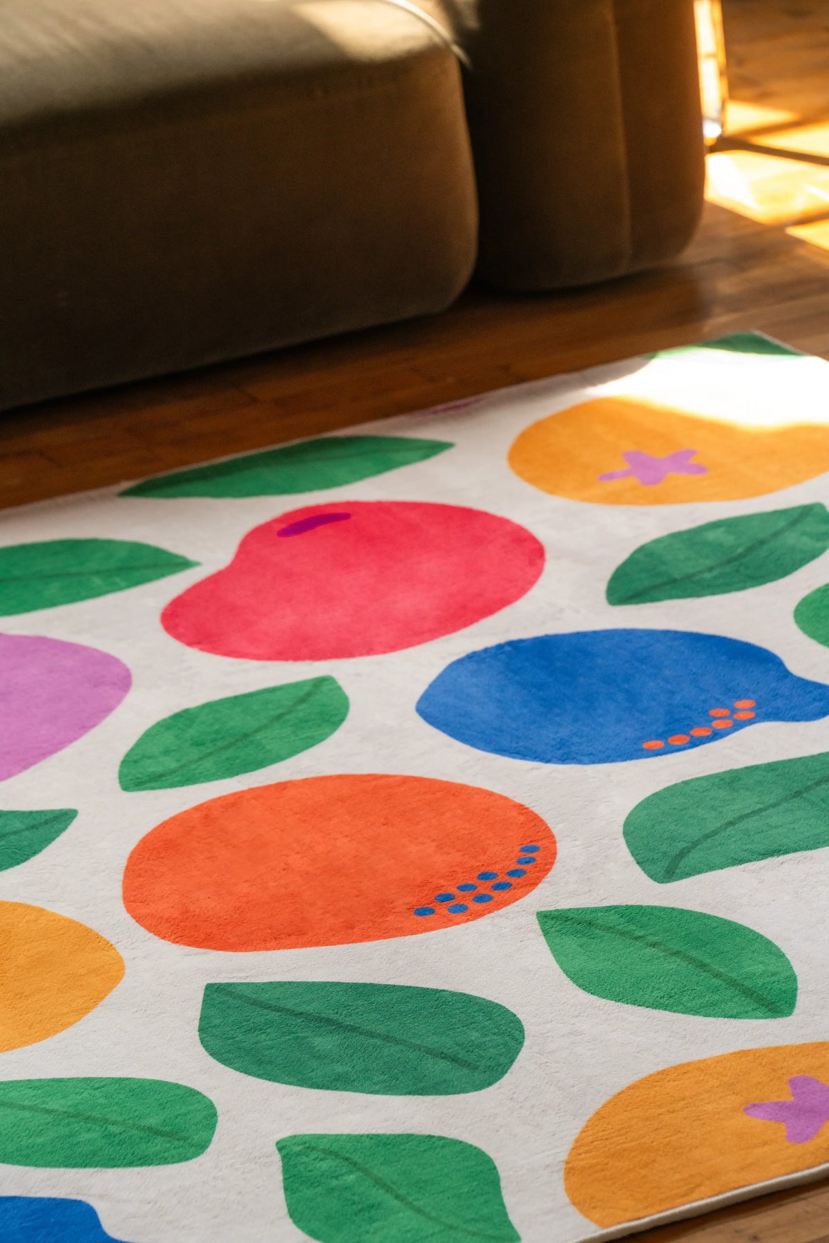 Pastel Fruit Party Rug by Becca Franks placed in front of a dark sofa on wood floor with natural light