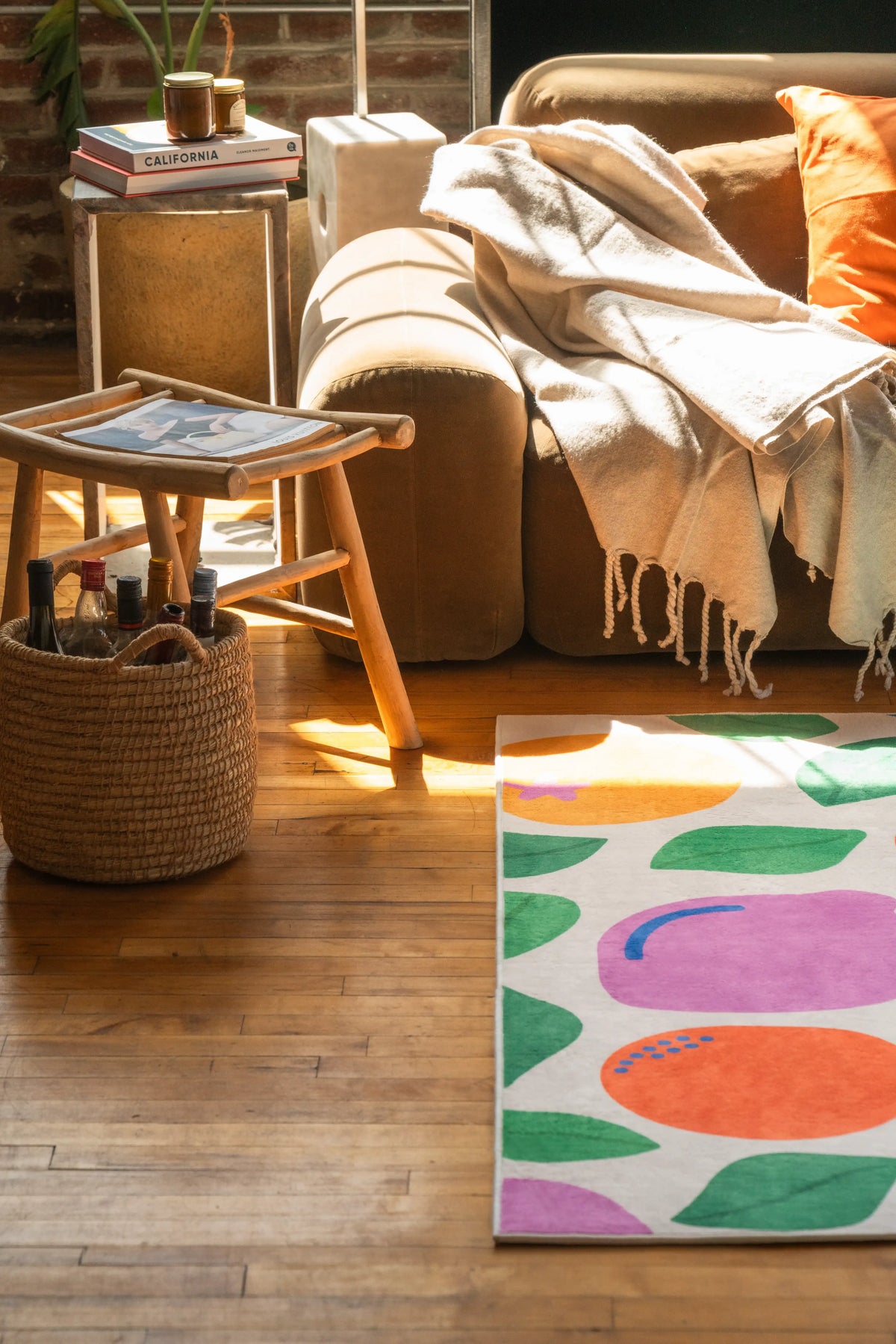 Pastel fruit party rug beside a sofa, partially lit by sun, with vibrant prints standing out on the wood floor