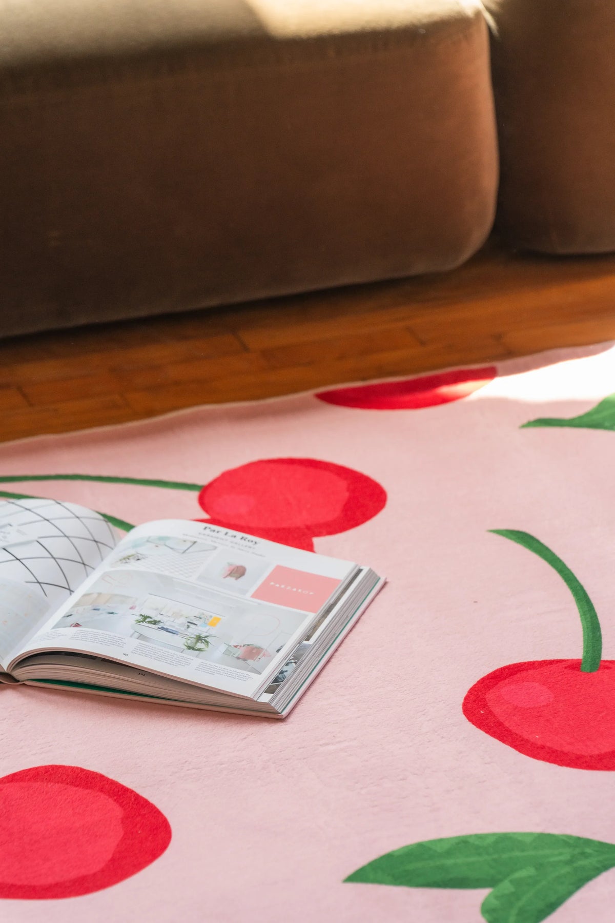 Close-up of an open book resting on a pink cherry rug with red fruit prints in a cozy reading nook