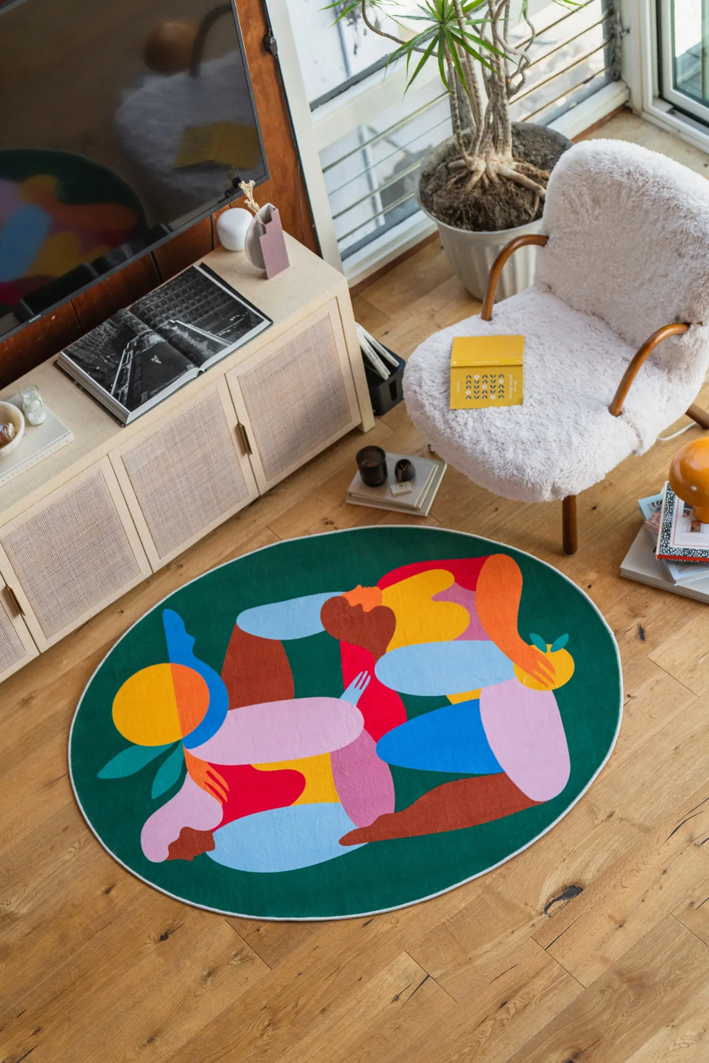 Oval Fruitvine Green Rug by Maggie Stephenson, styled in a bright corner with white boucle chair, books and houseplants