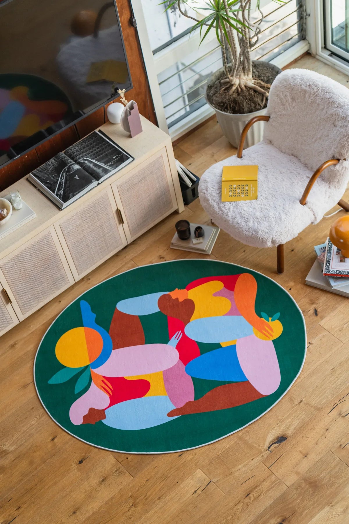 Oval Fruitvine Green Rug by Maggie Stephenson, styled in a bright corner with white boucle chair, books and houseplants
