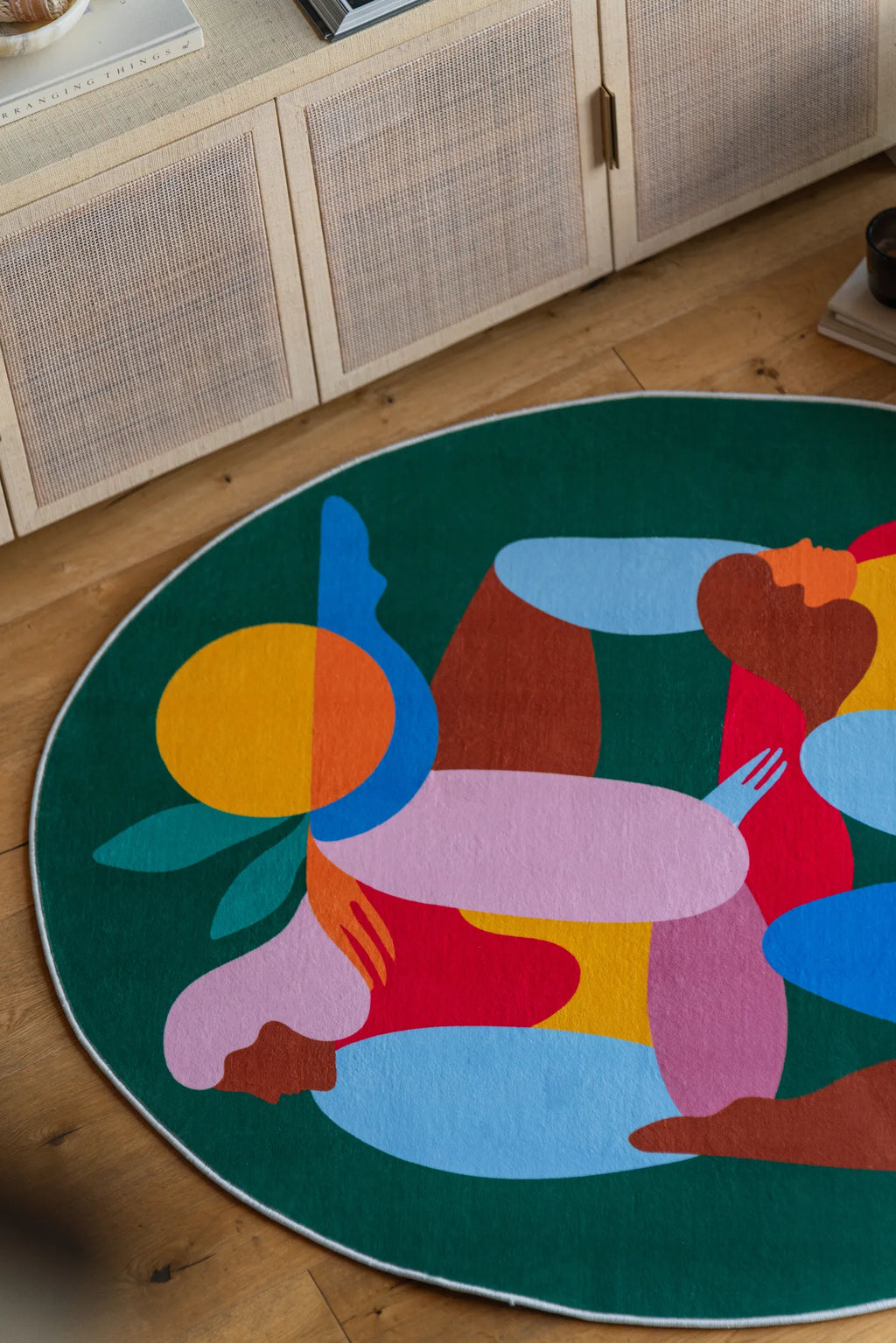 Top section of fruitvine green rug with abstract sun and figures placed near a woven cabinet.