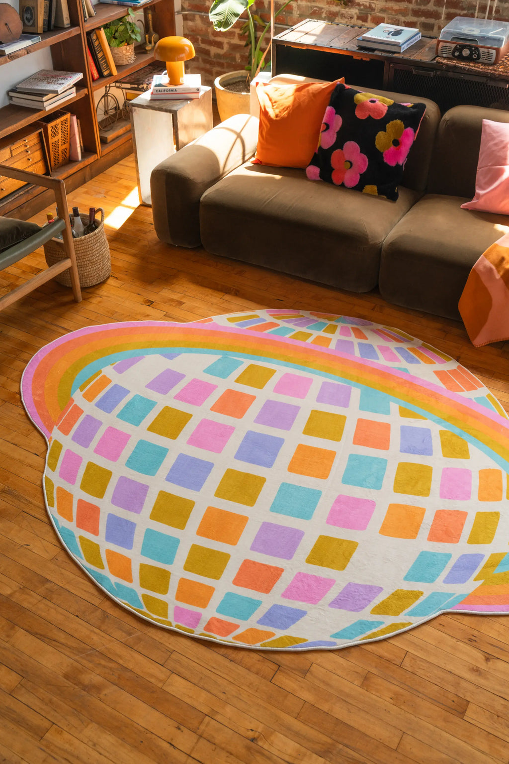 Planet-shaped rug in bold rainbow colors adds playful contrast beside a dark-toned couch on warm-toned wood floor.