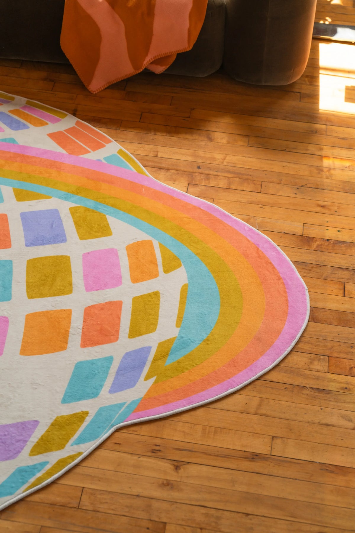 Partial view of the colorful disco checkered rug set near a sofa and against warm-toned hardwood floor