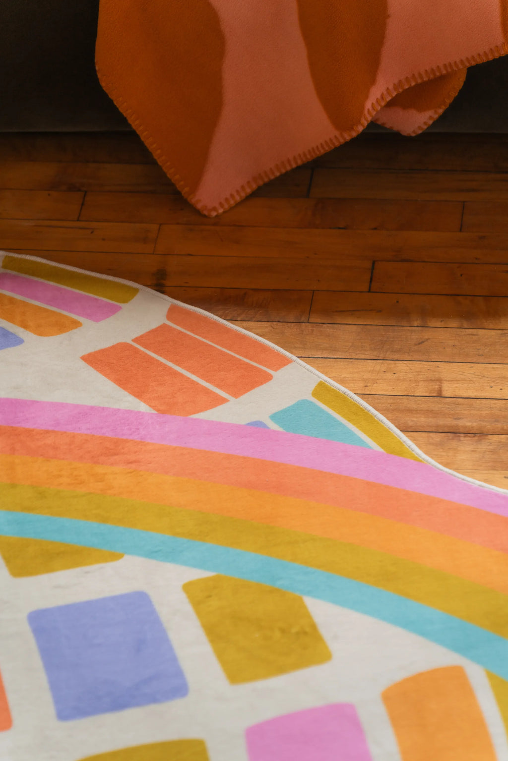 Detail of Colorful Disco Planet Checkered Rug by Darra Sargnt with curved rainbow border resting on wood floor