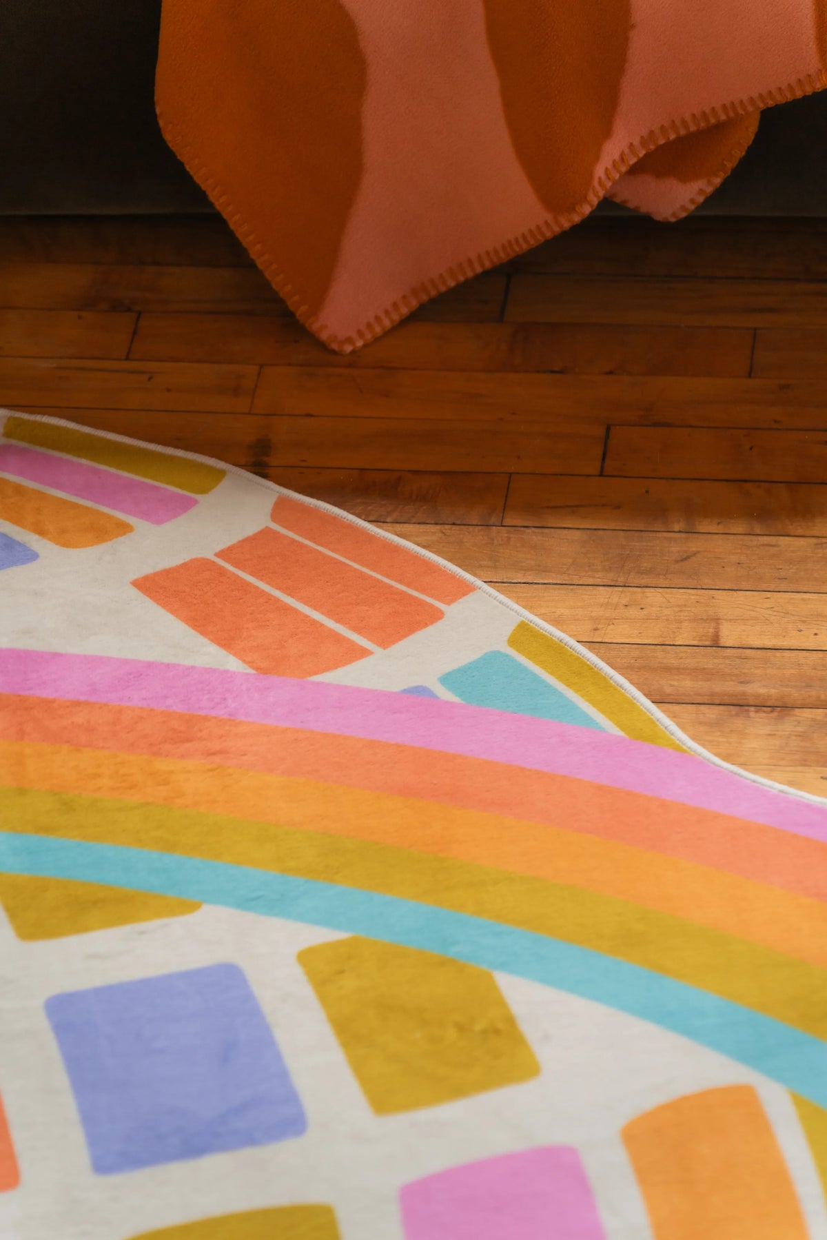 Detail of Colorful Disco Planet Checkered Rug by Darra Sargnt with curved rainbow border resting on wood floor