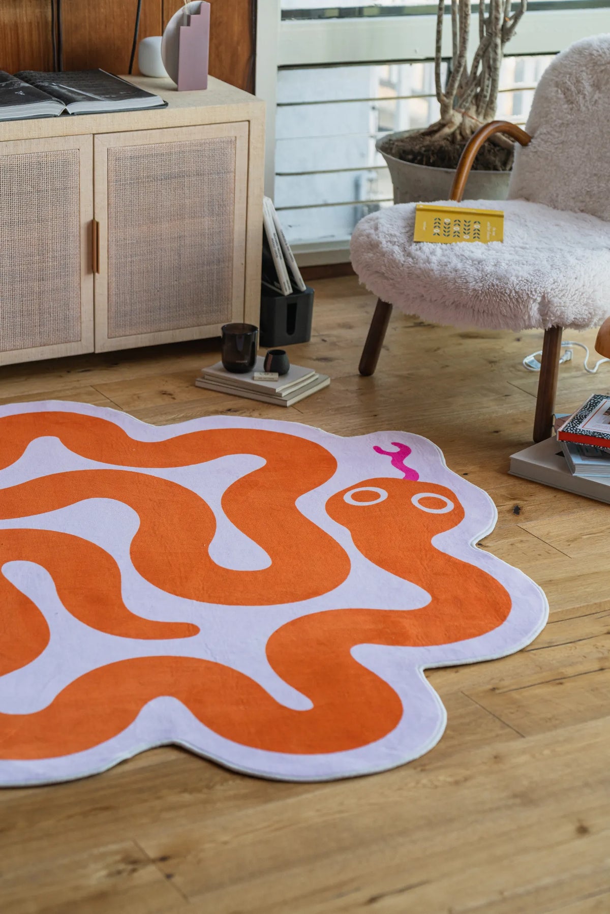 Orange snake rug laid out beside a fluffy chair and wooden cabinet in a sunlit modern room.