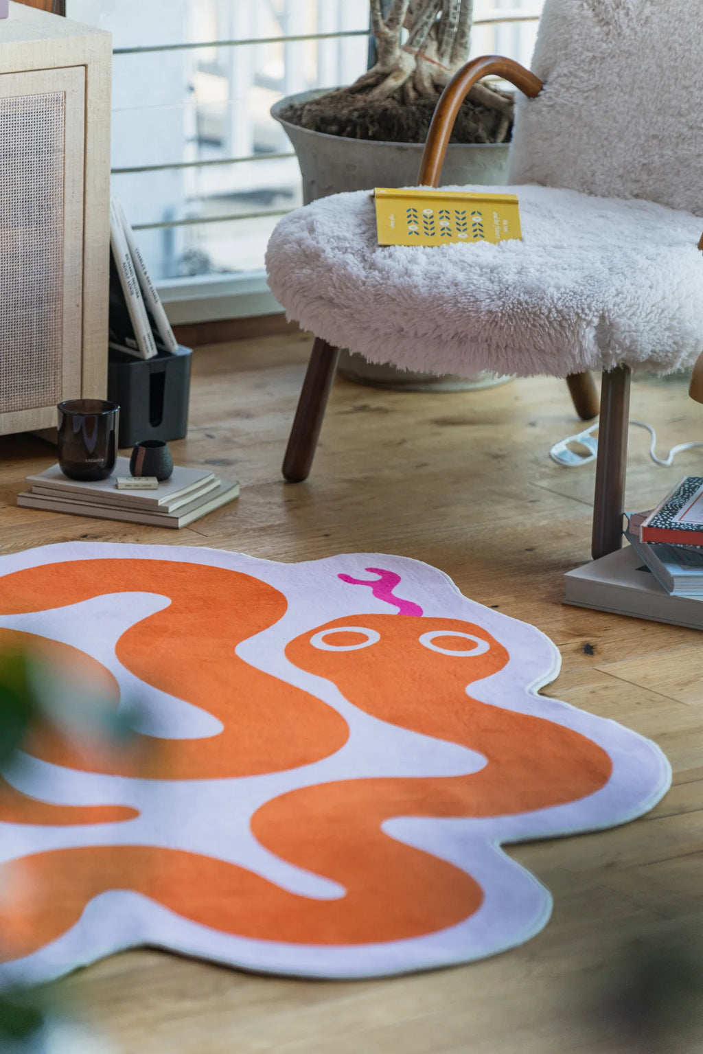 Close-up of the orange snake rug next to a fuzzy white chair and yellow book in a cozy wooden floor corner.