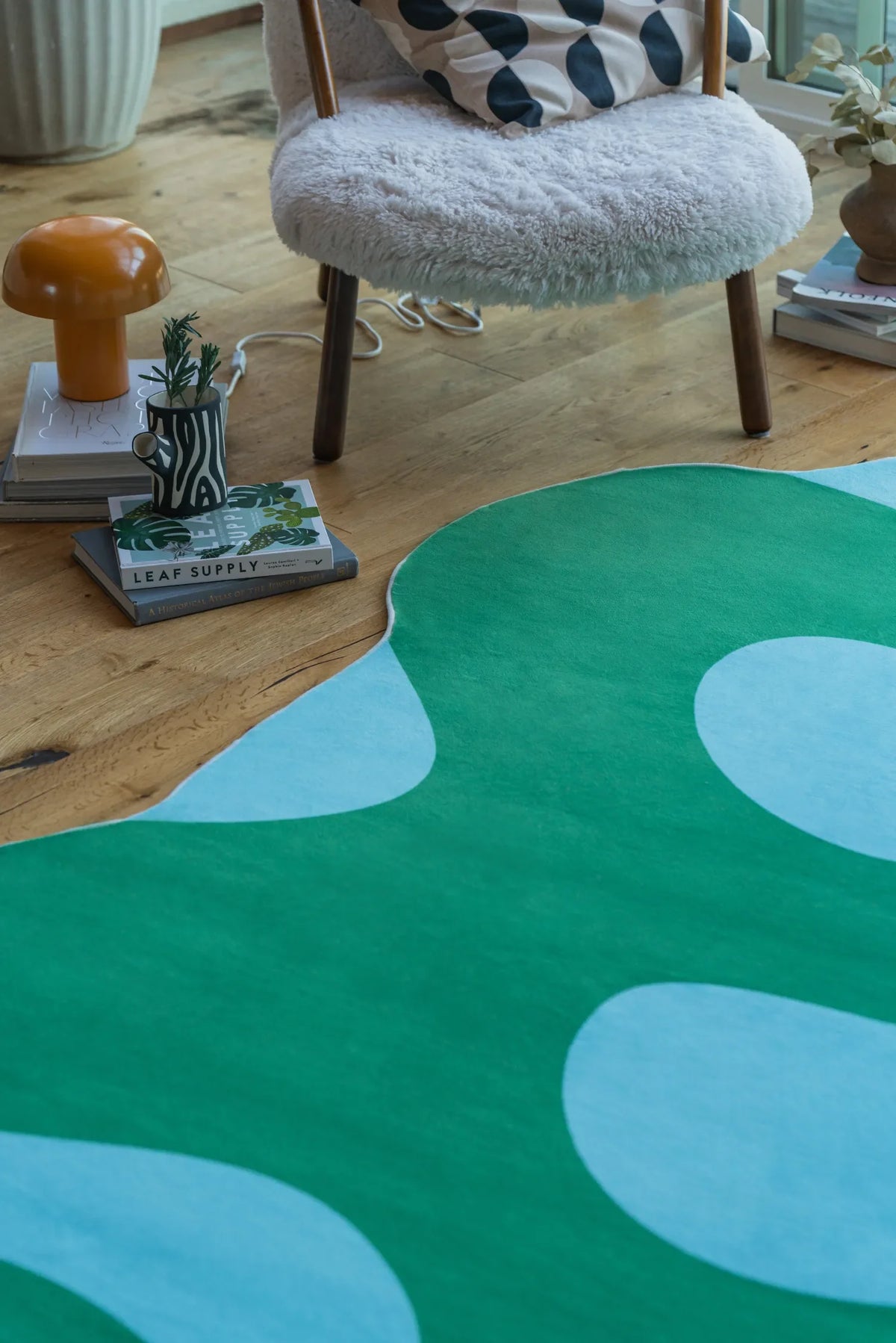 Close-up of the irregular green moss rug next to a boucle chair, styled with a polka dot pillow, books, and ceramic accents.